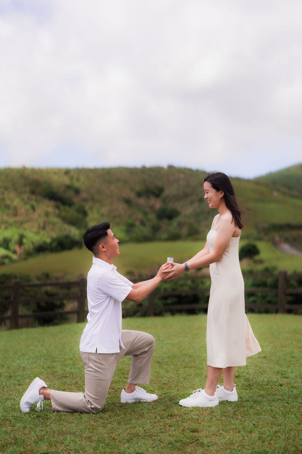 A romantic proposal scene on a grassy hillside with rolling green mountains in the background at Taiwan's Qingtiangang Grassland.