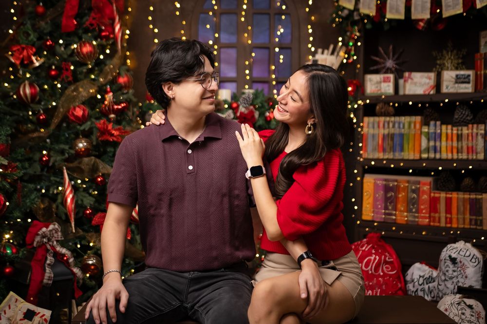 A couple shares a joyful moment together in front of a decorated Christmas tree and bookshelf with festive holiday decor.