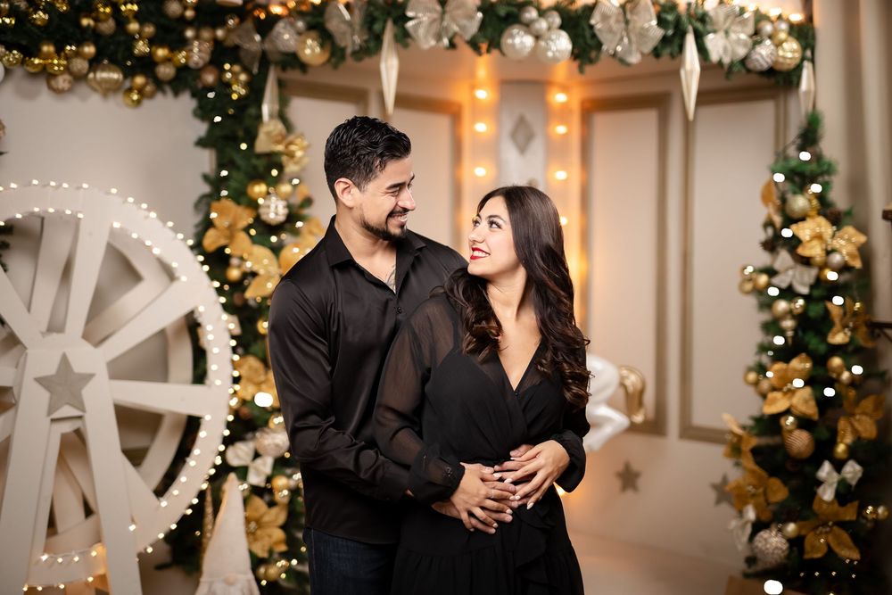 A couple in formal black attire shares romantic moments in front of decorated Christmas trees and twinkling lights.