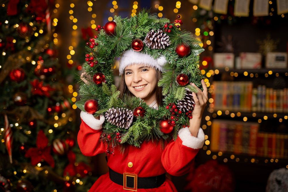 A festive Christmas display with decorated evergreen branches, pinecones, red ornaments, and twinkling lights in a cozy setting.