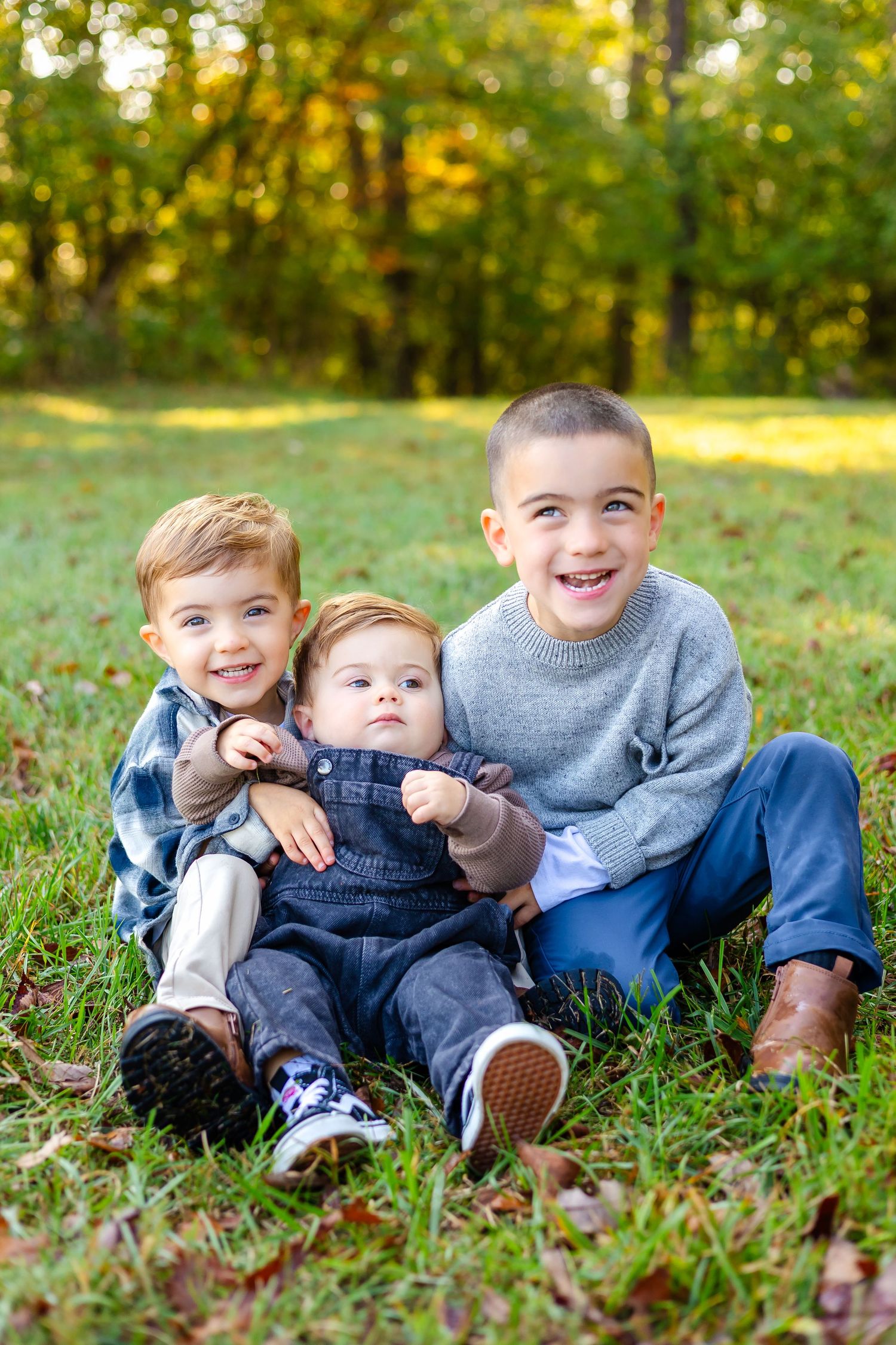 Three children laying in autumn grass wearing denim and casual clothes on a sunny day.
