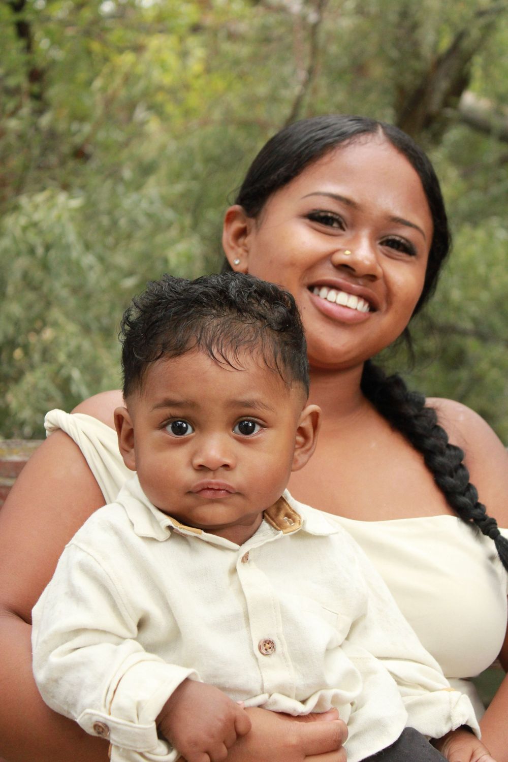 A parent and child wearing cream-colored outfits share joyful expressions while posing together outdoors.
