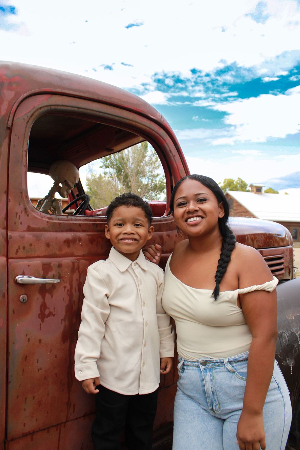 Family poses together in front of a rustic vintage truck on a sunny day with blue skies and clouds.