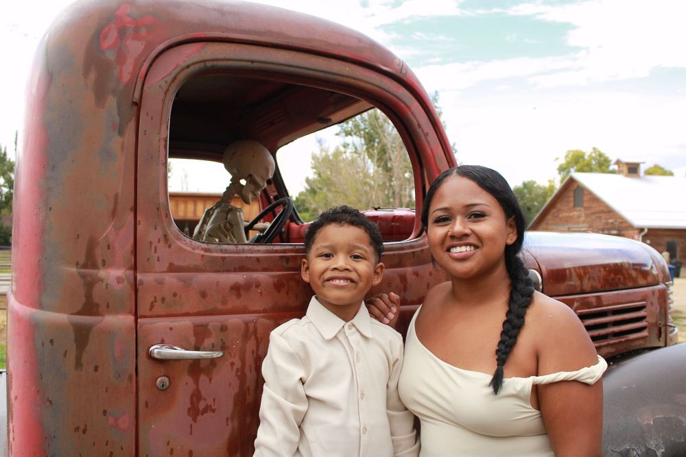 A group poses playfully in front of a rustic vintage red pickup truck in a sunny outdoor setting.