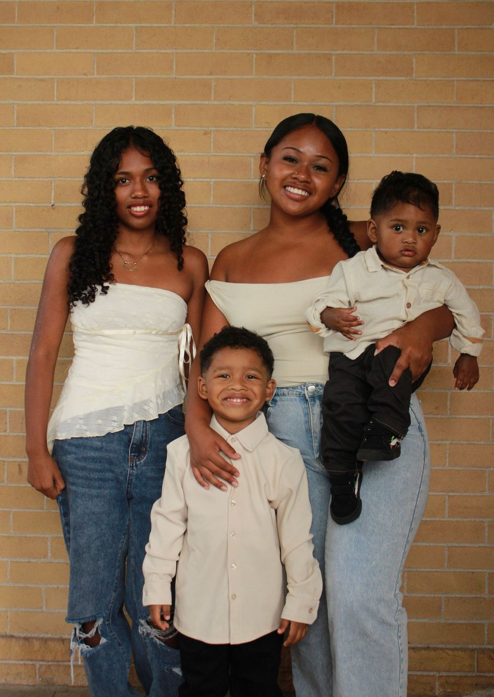 Four candid photos against a brick wall show joyful expressions and casual outfits of blue jeans and white shirts.
