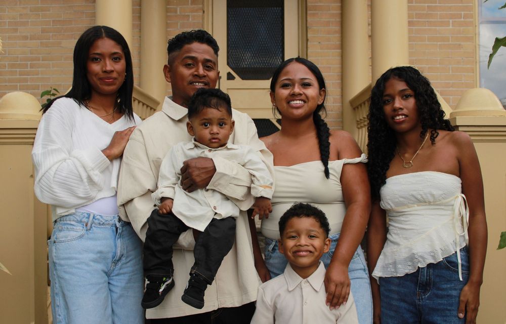 A family group in casual attire poses together on stone steps outside a building.
