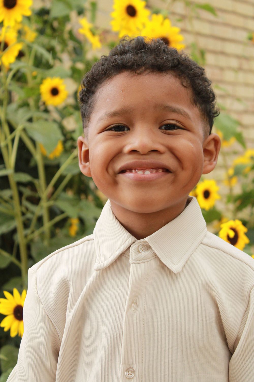 A bright smile radiates against a backdrop of cheerful yellow sunflowers in a garden setting.