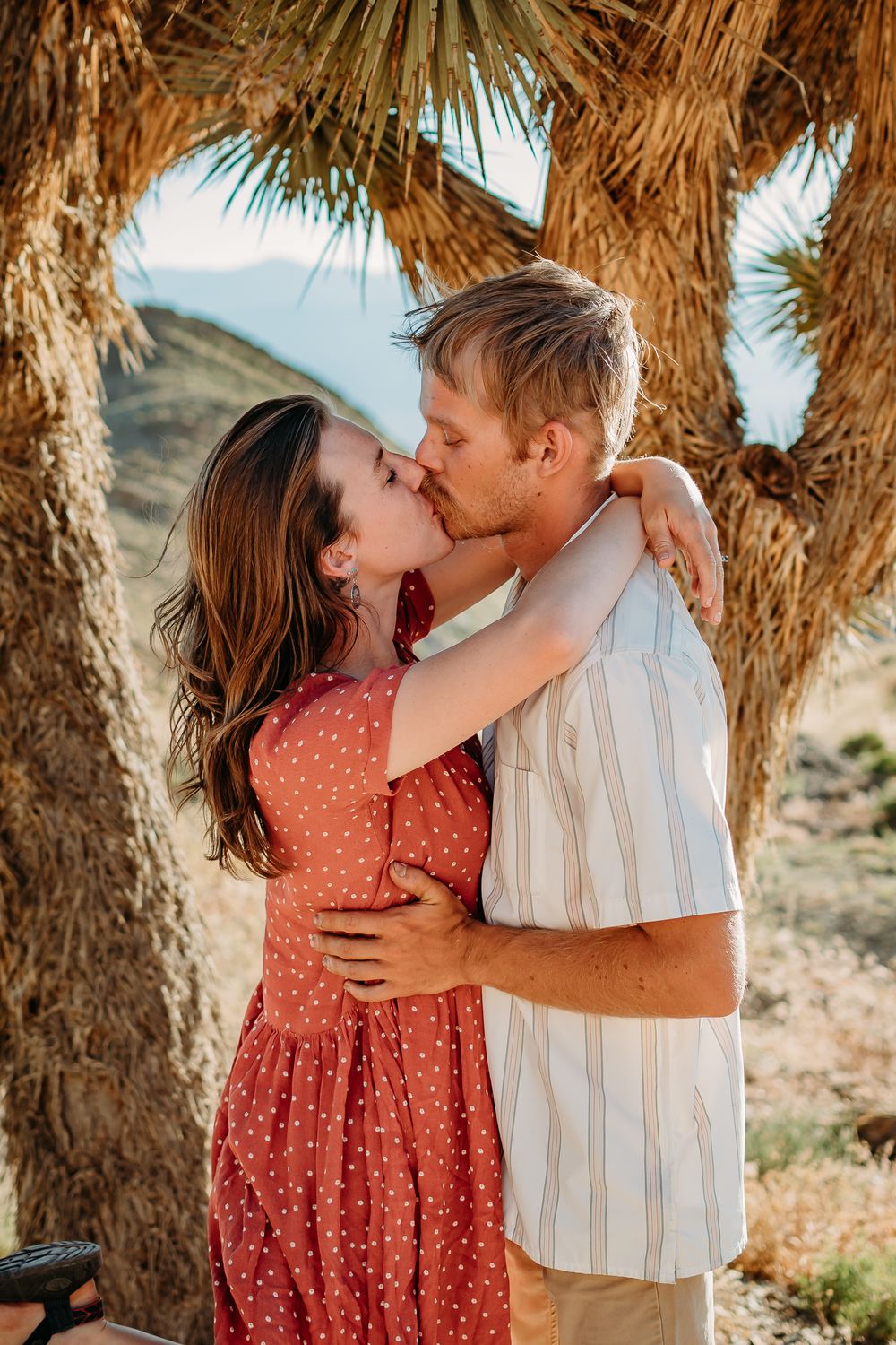 Couple sharing tender kisses beneath palm trees in desert landscape.