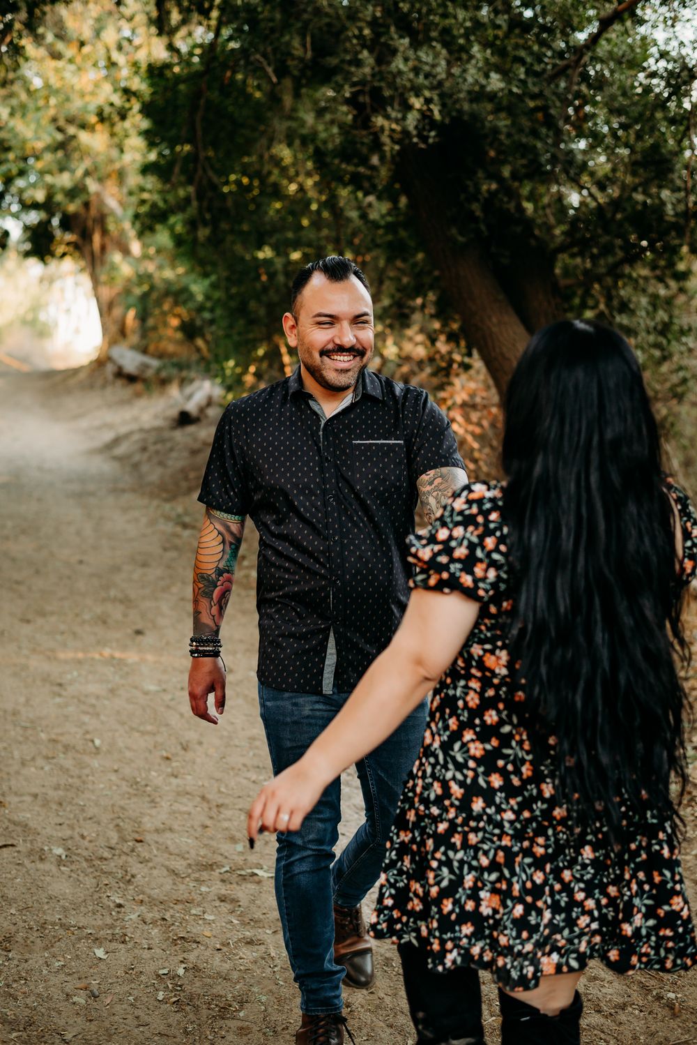 Couple walks hand in hand through a park wearing casual floral and polka dot outfits.