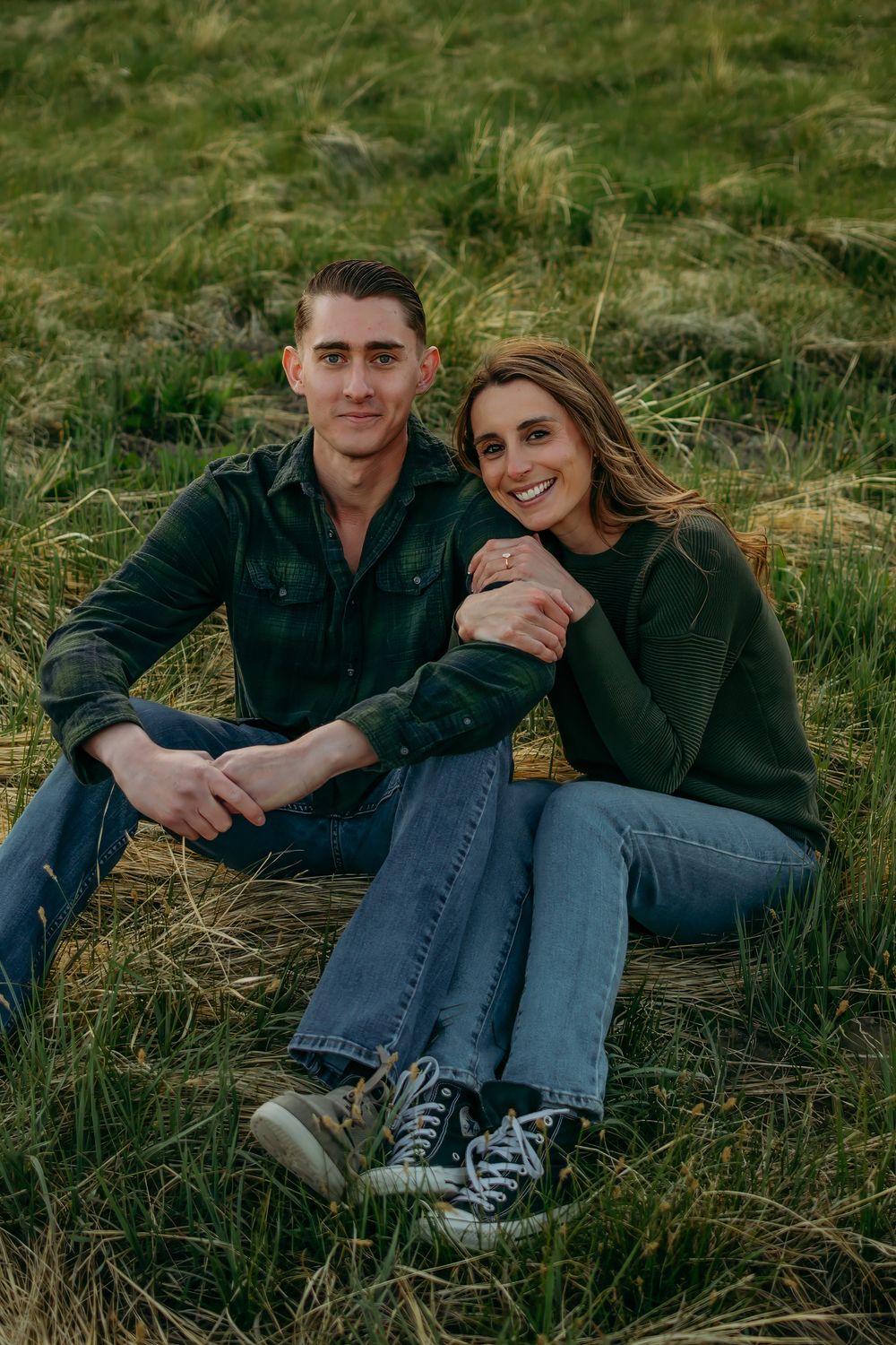 Casual couple relaxing in grassy field during outdoor photoshoot.
