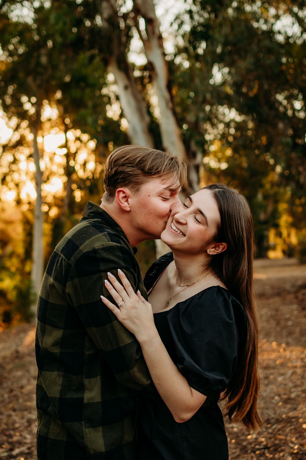 Couple embraces tenderly in a golden-lit forest setting during sunset.