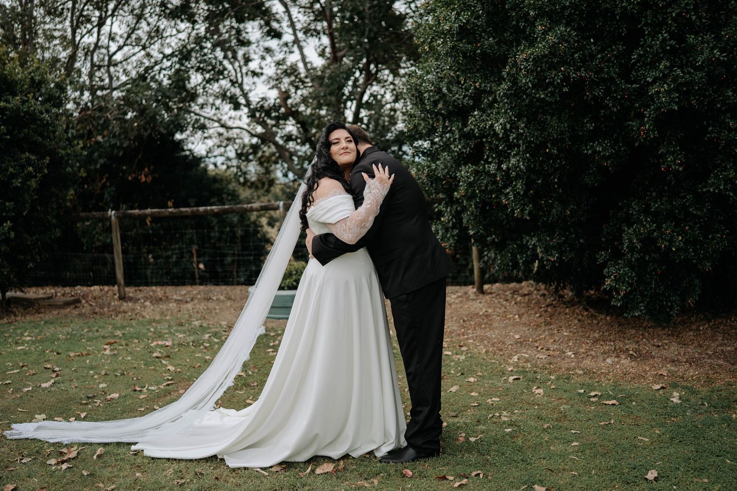 A romantic wedding couple shares an intimate moment in a lush garden setting with a flowing white dress trailing behind them.