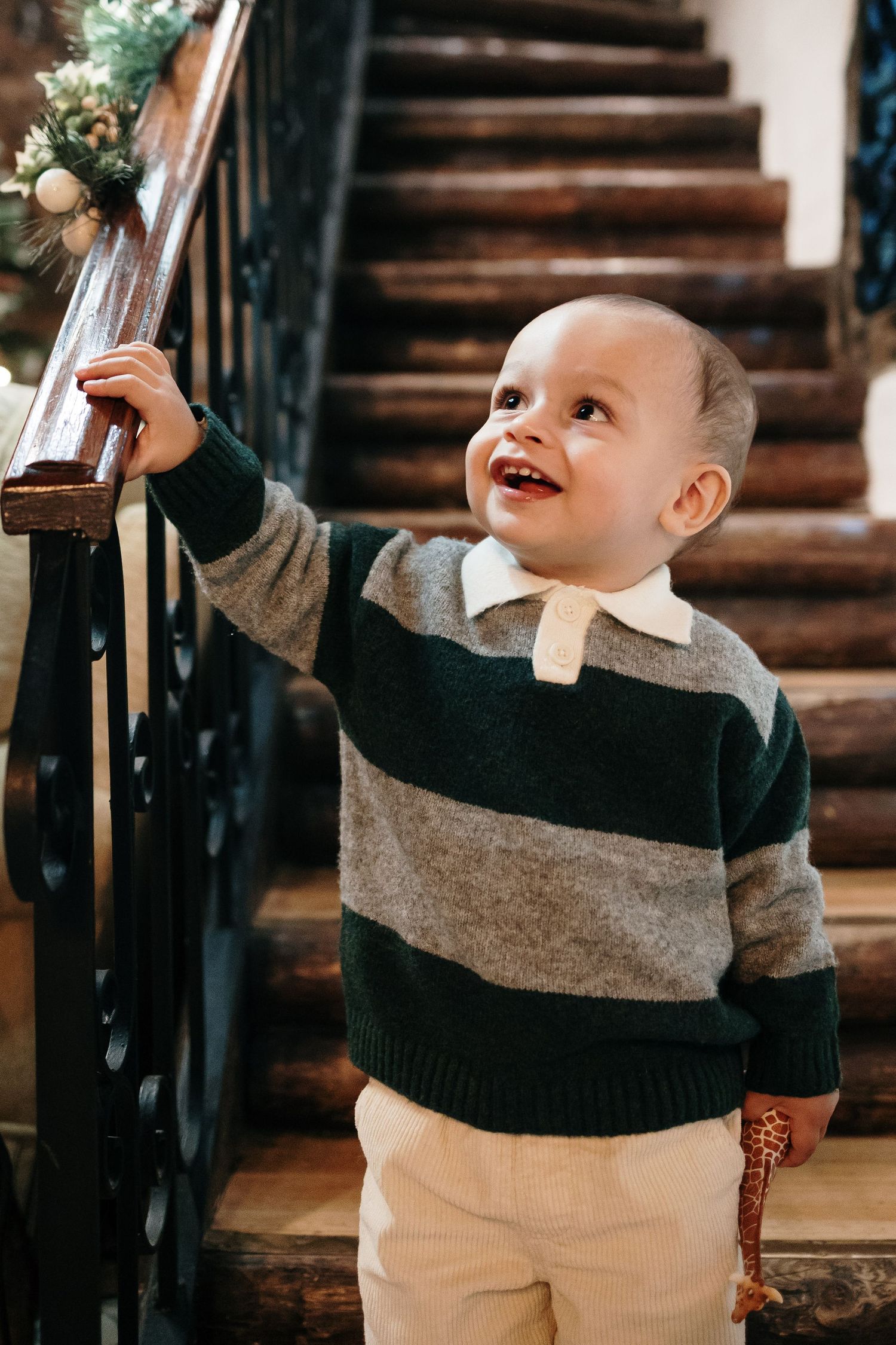 Child in striped sweater playing near wooden staircase with festive holiday decorations.