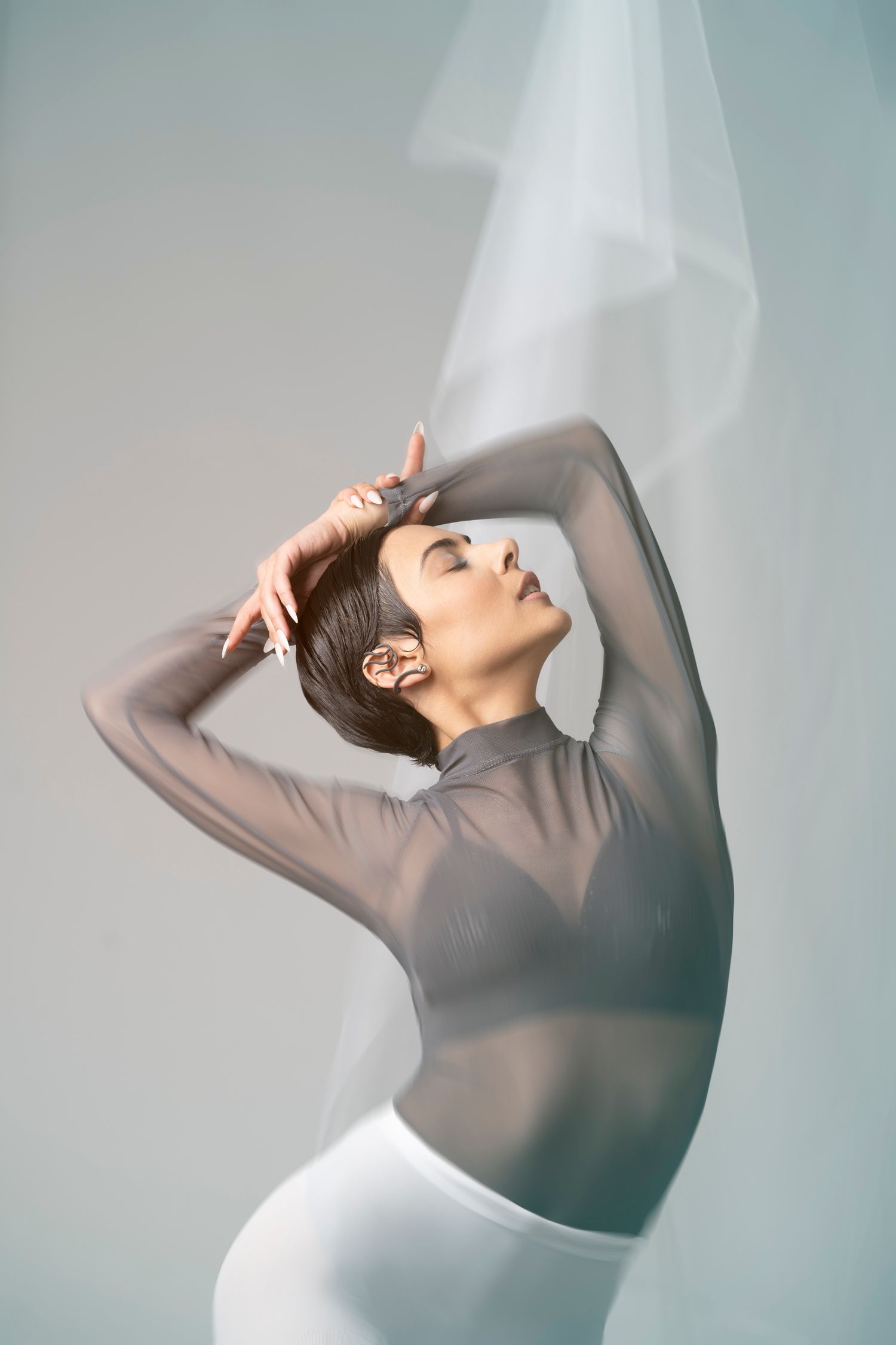 Studio portrait of a woman in a sheer top with a white veil or fabric; high-end movement and fashion photography.