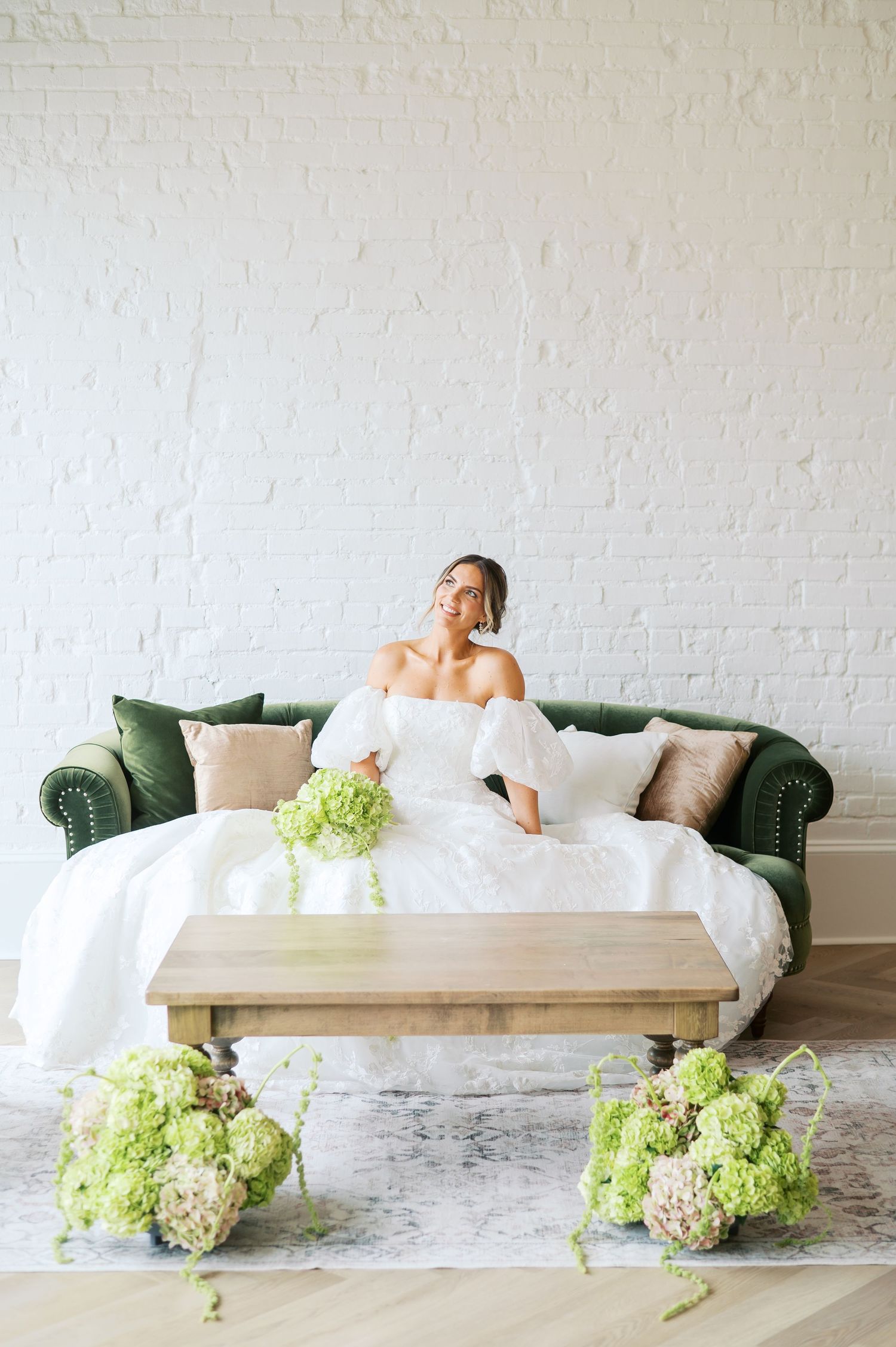 Elegant boudoir photo series showing a figure draped in white linens on a green velvet couch with hydrangea flowers.