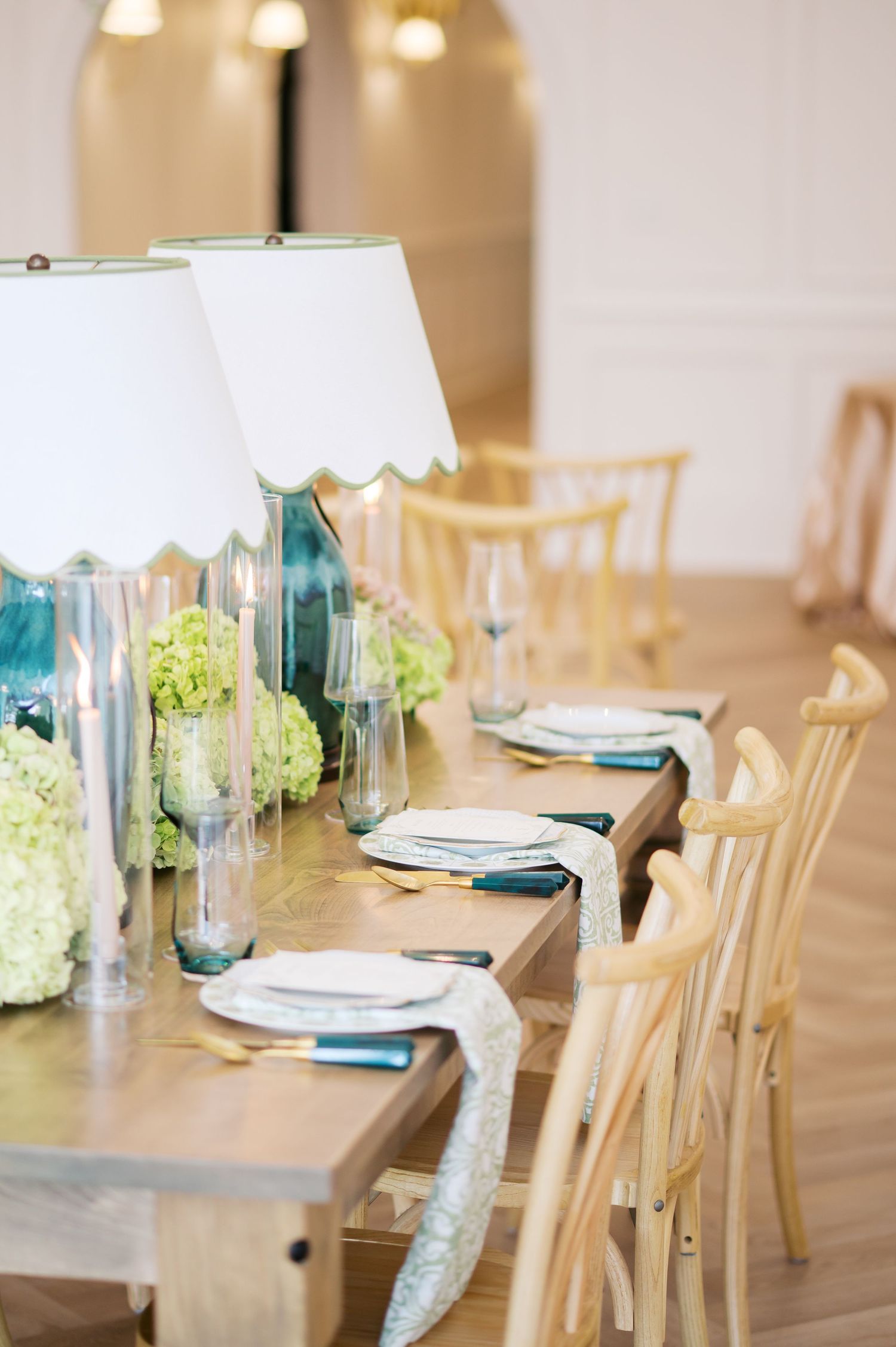 Elegant dining table setting with white chairs, blue accents, and natural light streaming through windows in a coastal style room.