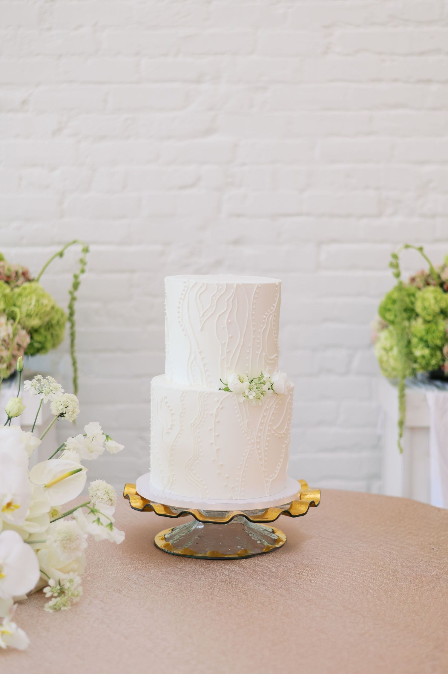 Four elegant white wedding cakes with textured frosting displayed on a beige surface with delicate floral accents.