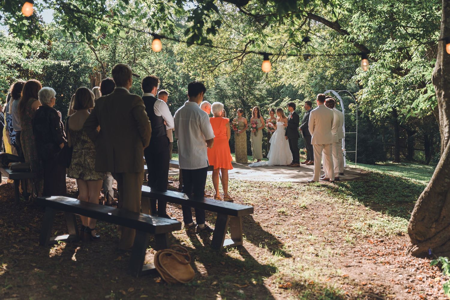 A group of people gather outdoors in a wooded area during a daytime event.