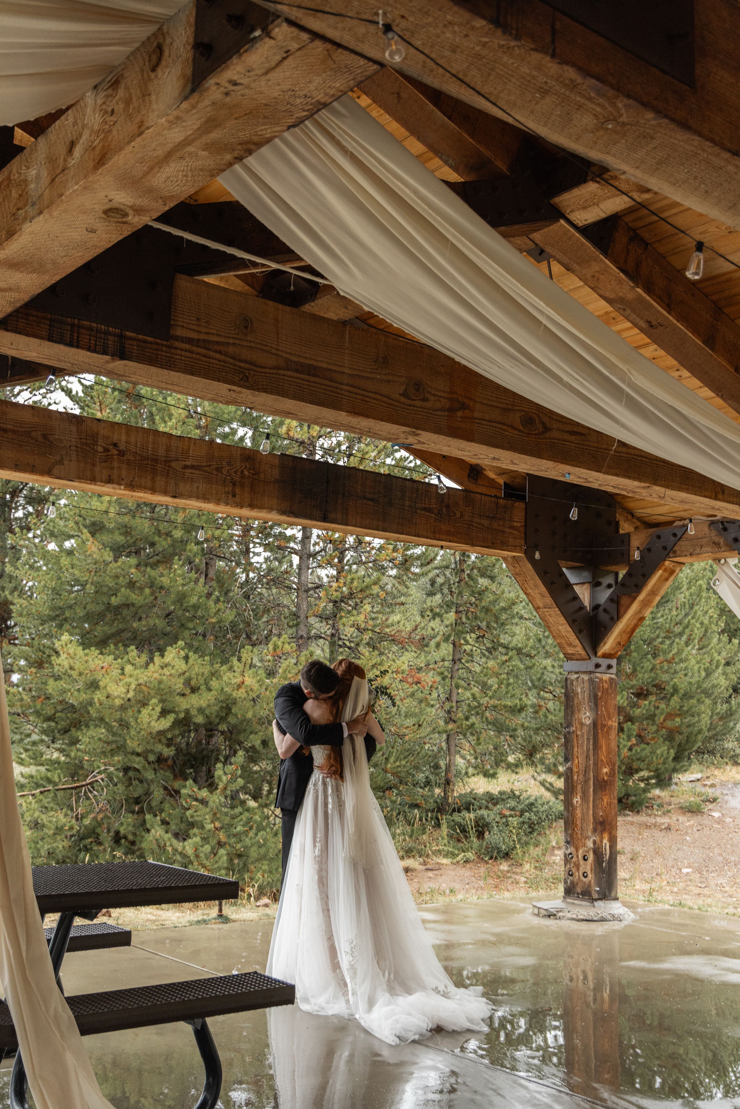 White fabric drapes elegantly from wooden beams over a rustic outdoor pavilion overlooking a serene pond.