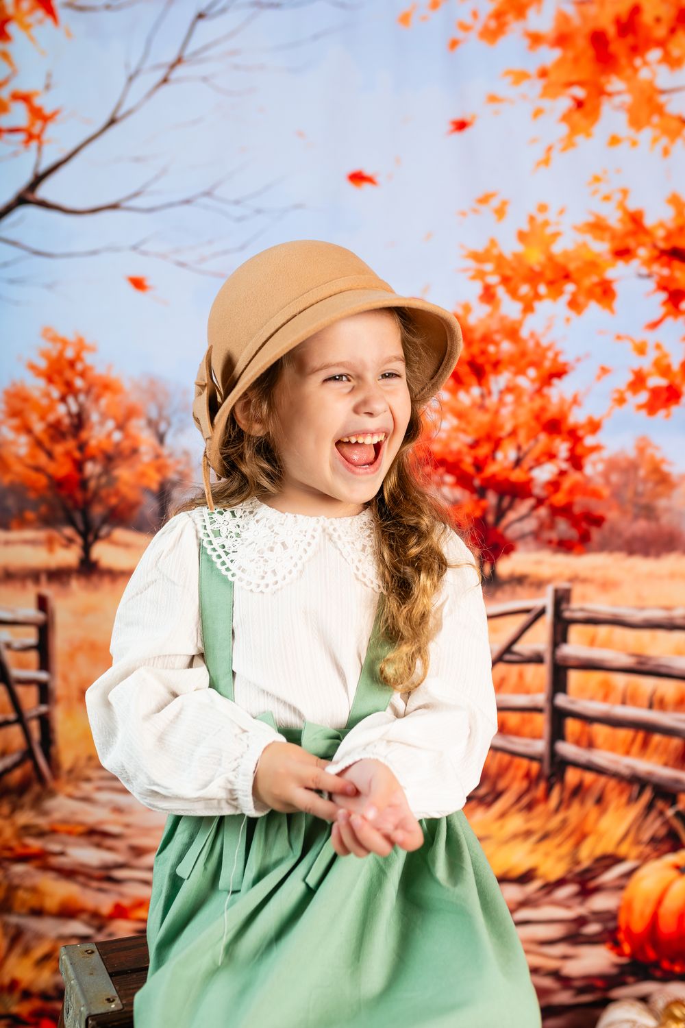 A cheerful autumn scene with a white blouse, green dress, and tan hat against vibrant orange fall foliage.