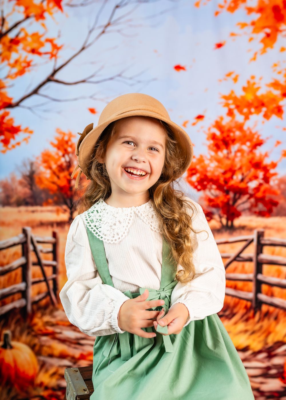 A child in autumn attire with a beige hat and green pinafore dress poses against a backdrop of vibrant fall foliage.