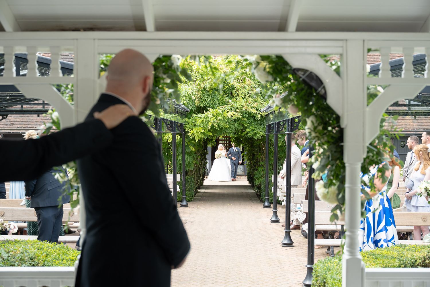 The bride enters the aisle for their outdoor wedding ceremony as her groom looks up the aisle as he waits for her to join him.