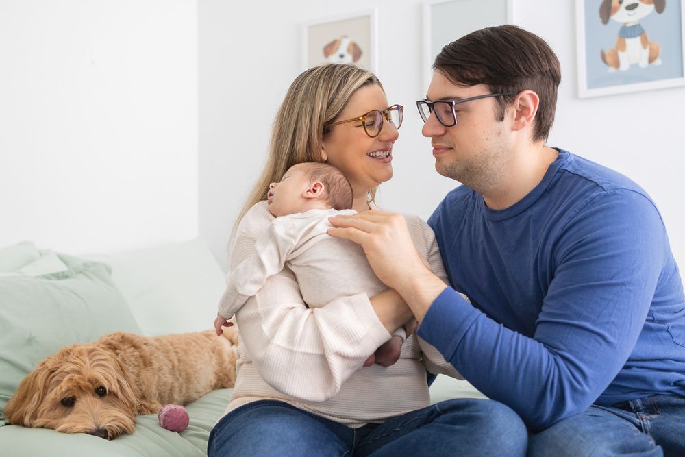 A couple sits on a couch with their golden retriever dog, sharing a tender moment in a bright room with wall art.