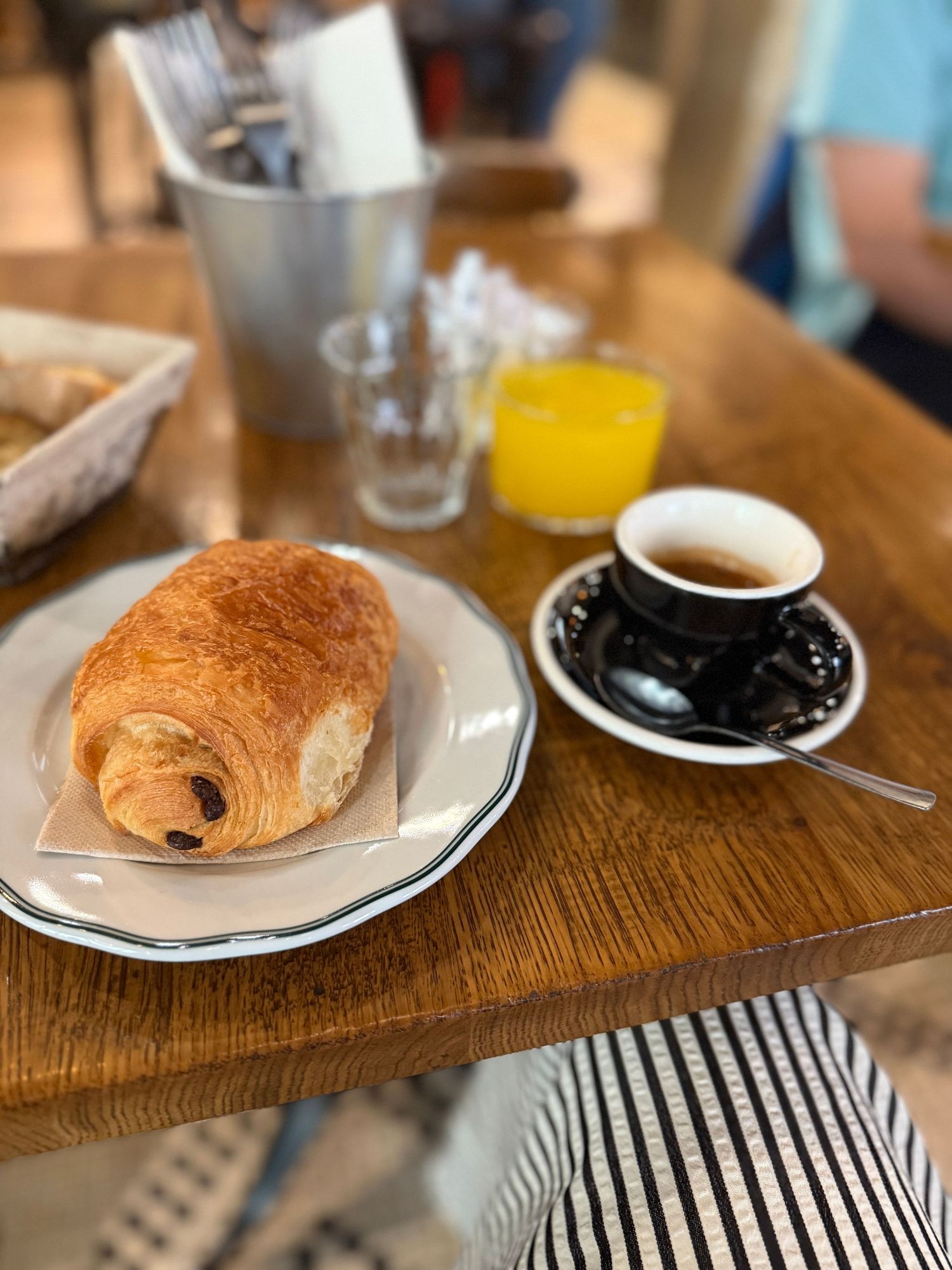 Breakfast setting with croissants and coffee on wooden table with striped napkin.