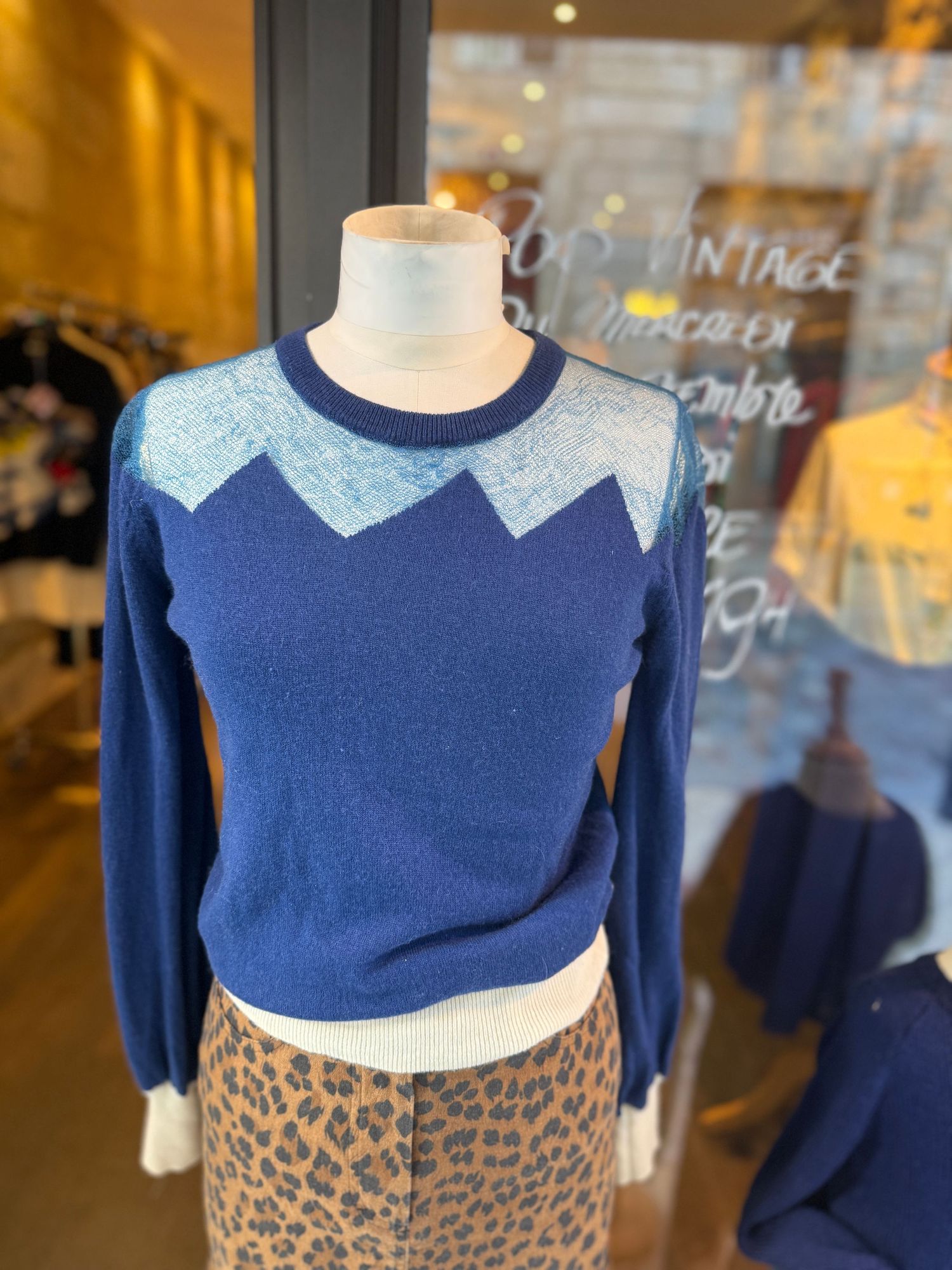Display of blue and gray color block sweaters on mannequins in shop window.