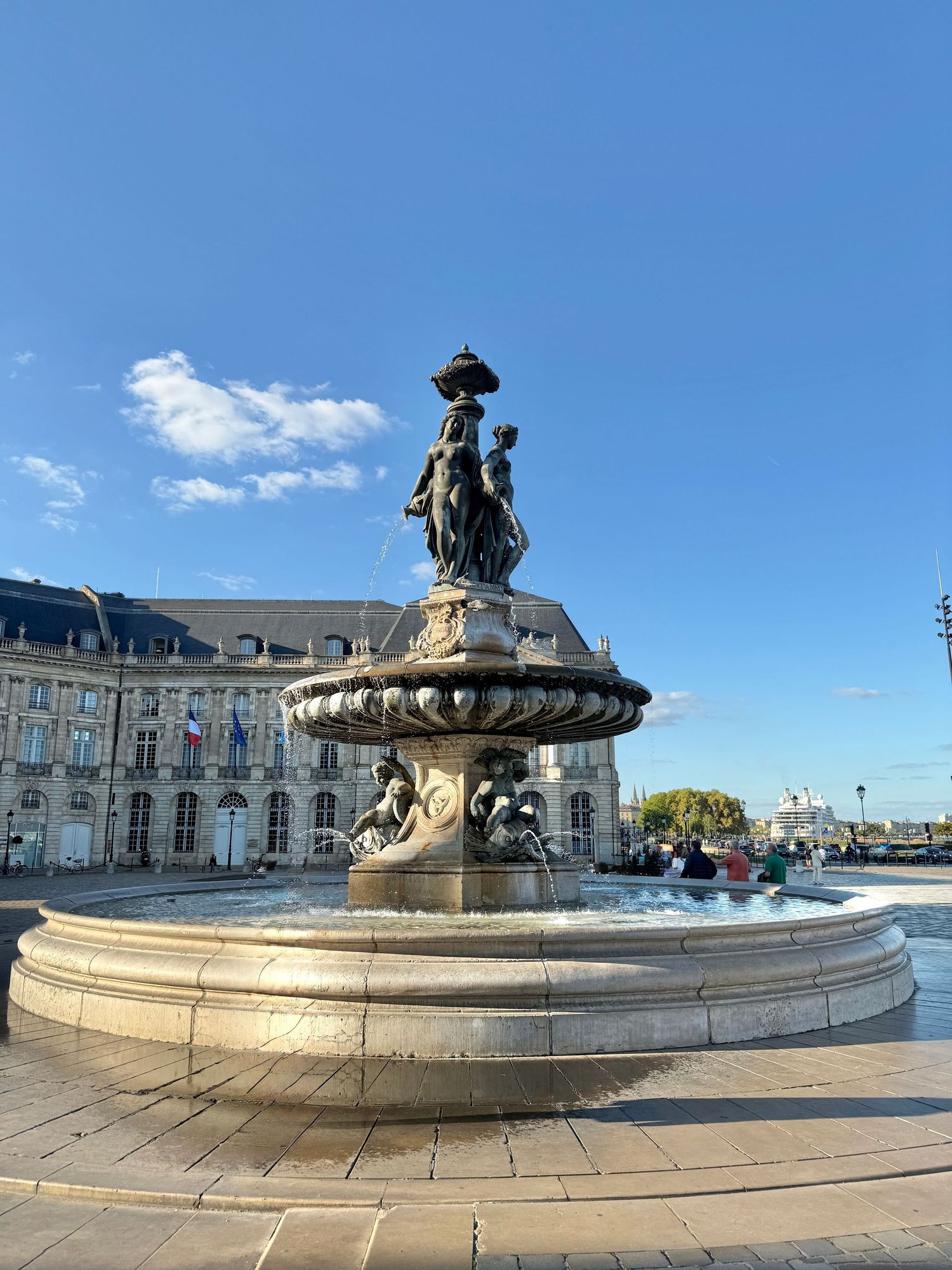 Grand ornate fountain with classical sculptures in a public square under blue sky.