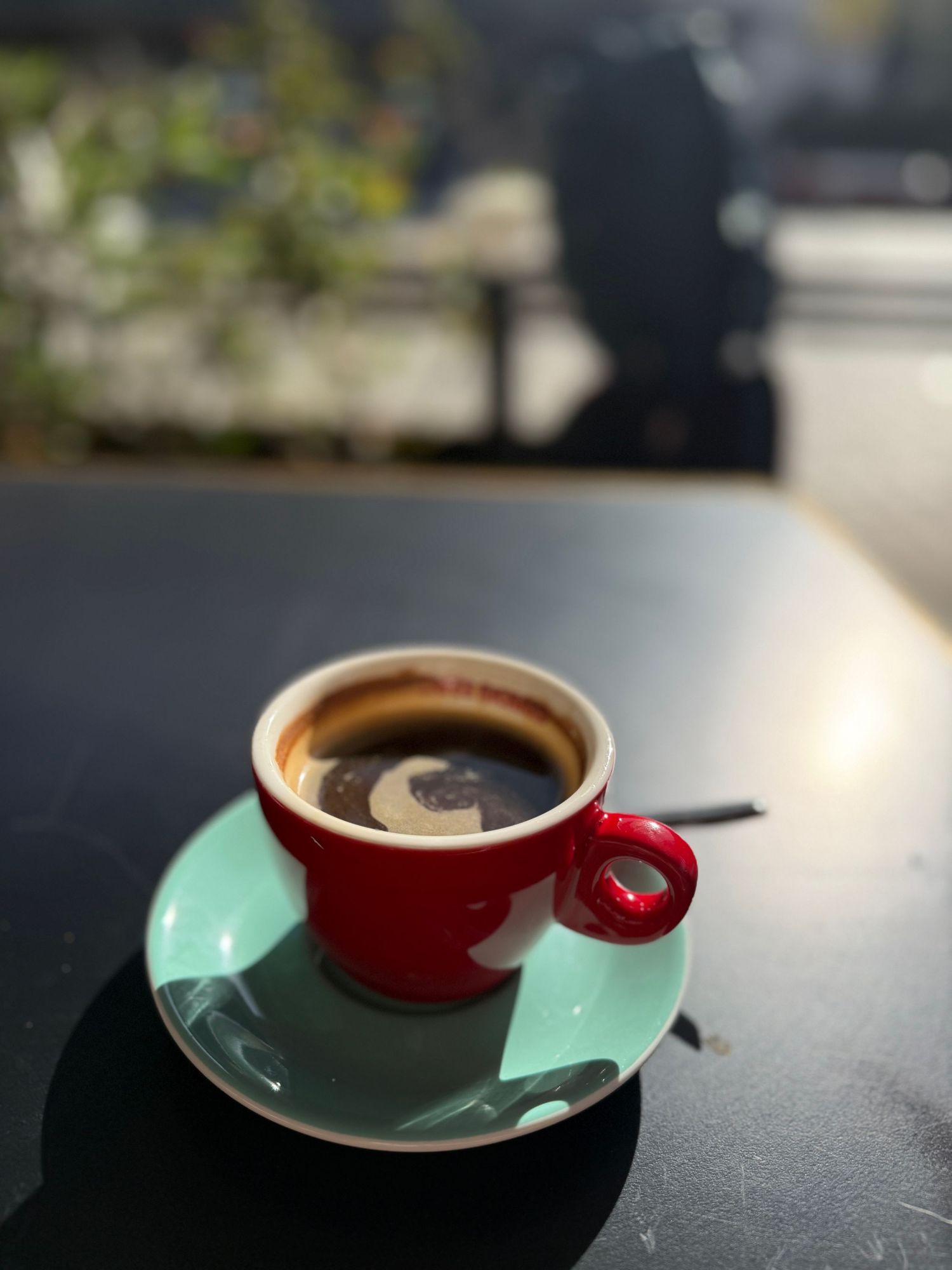 Red coffee cup with saucer on a dark surface in natural lighting.