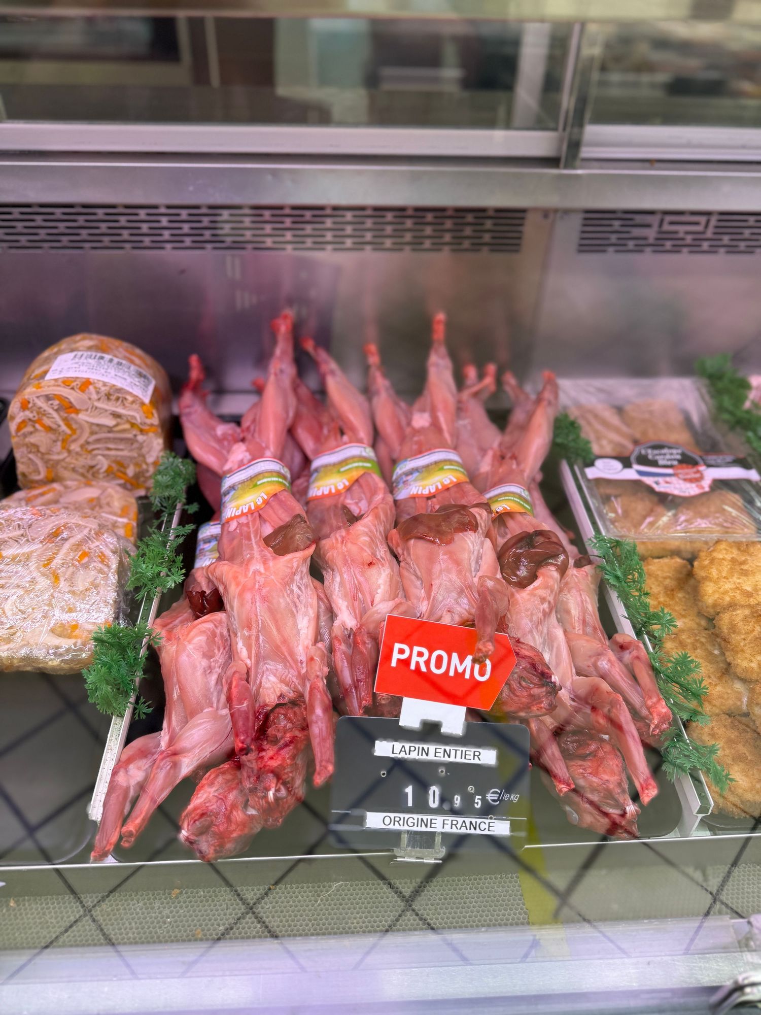 Display case of raw meat cuts and promotional signs in a butcher shop.