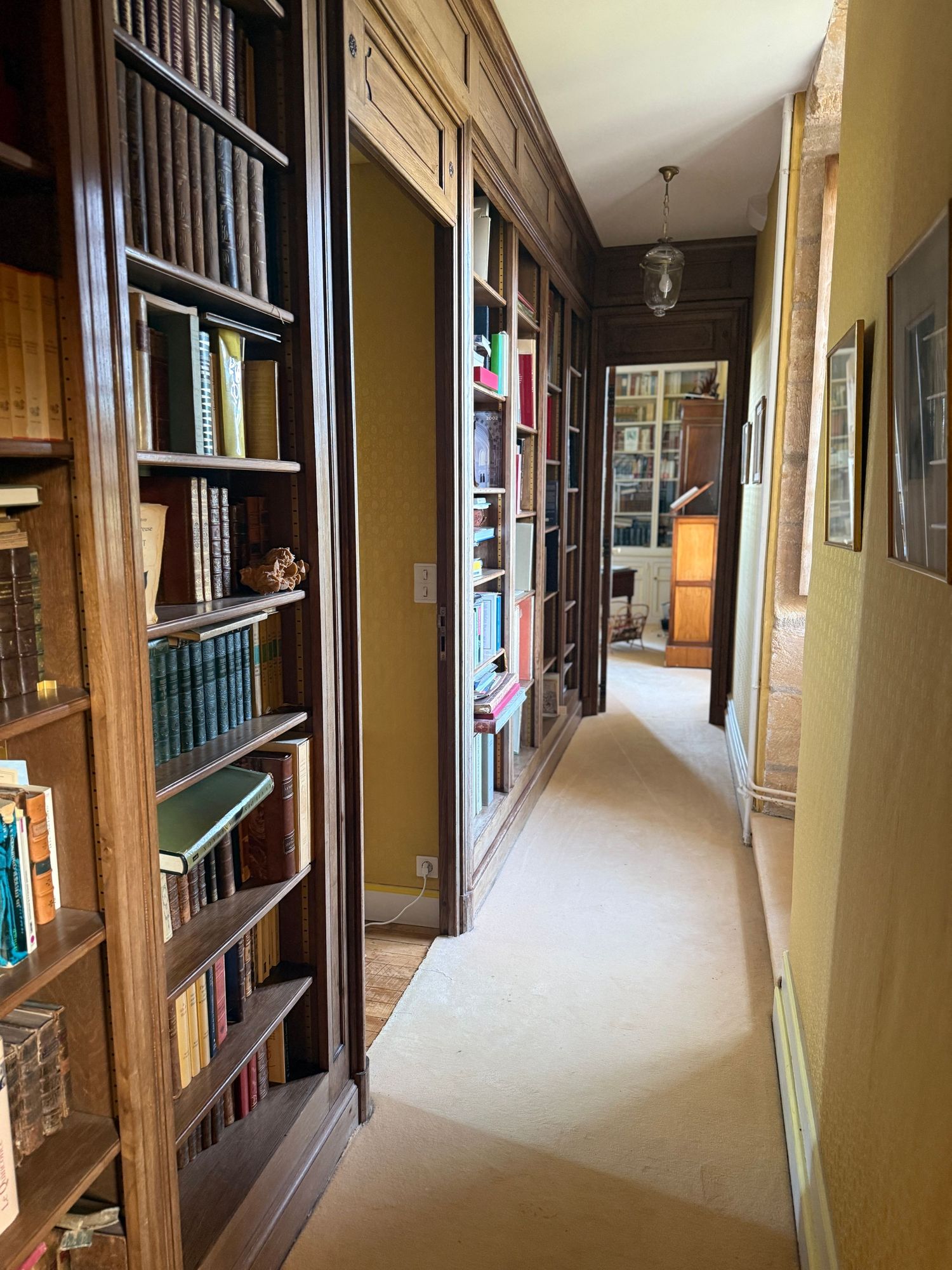 Long hallway with wooden bookshelves and cream walls in traditional library setting.