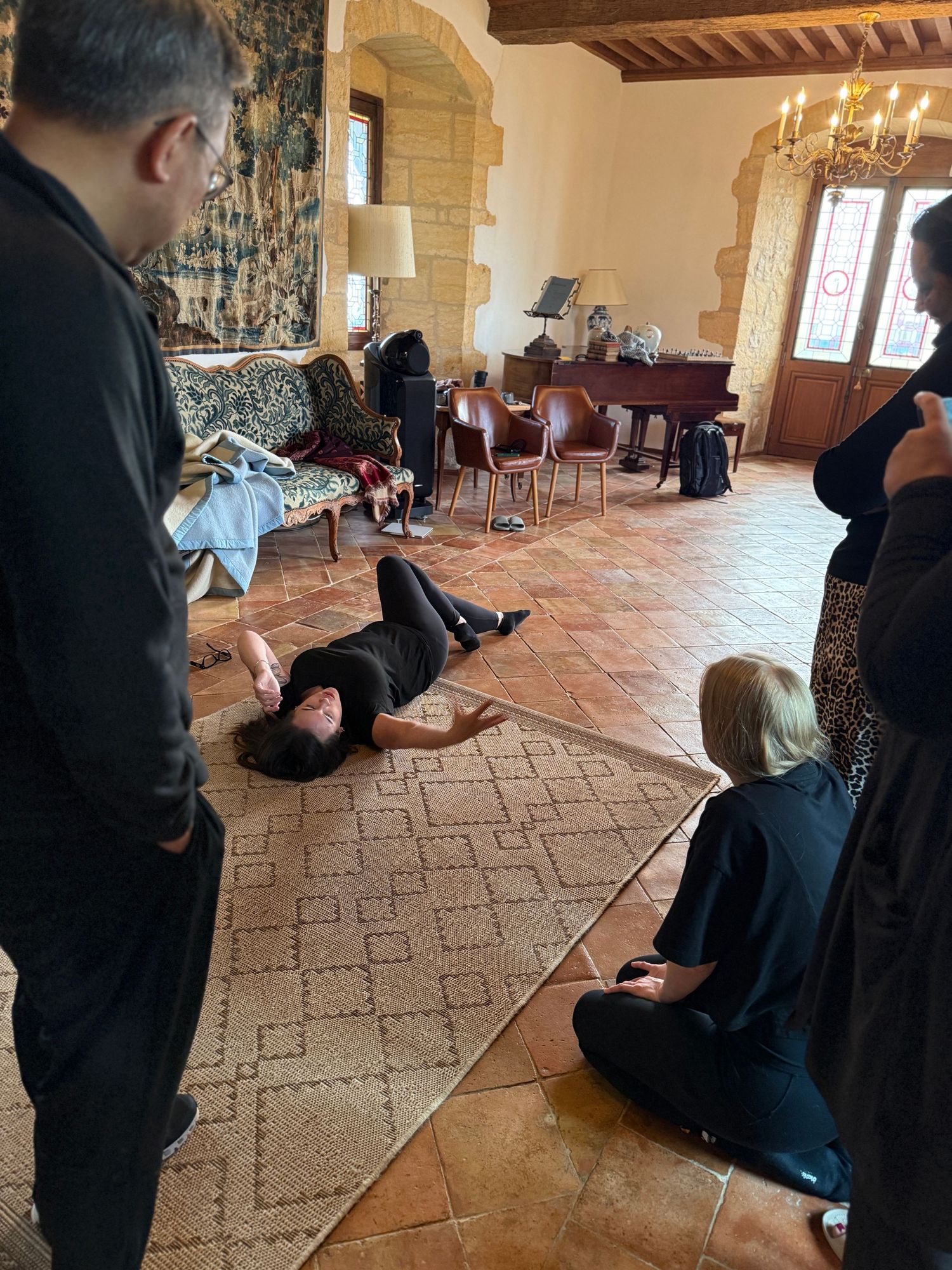 People gathered in an elegant room with stone walls and patterned carpet during a theatrical performance.