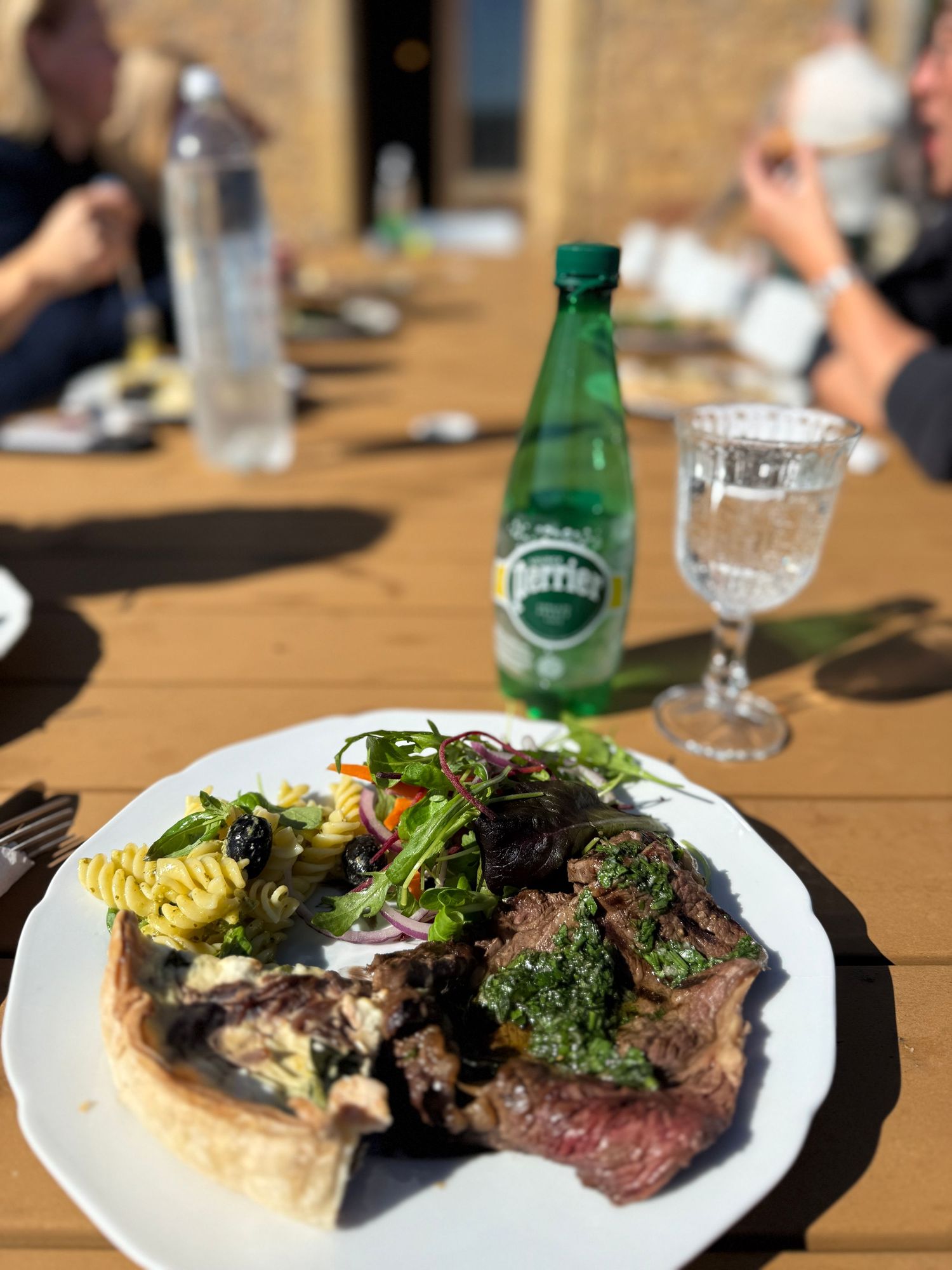 Grilled steak with vegetables and salad on white plate next to Perrier bottle and wine glass.
