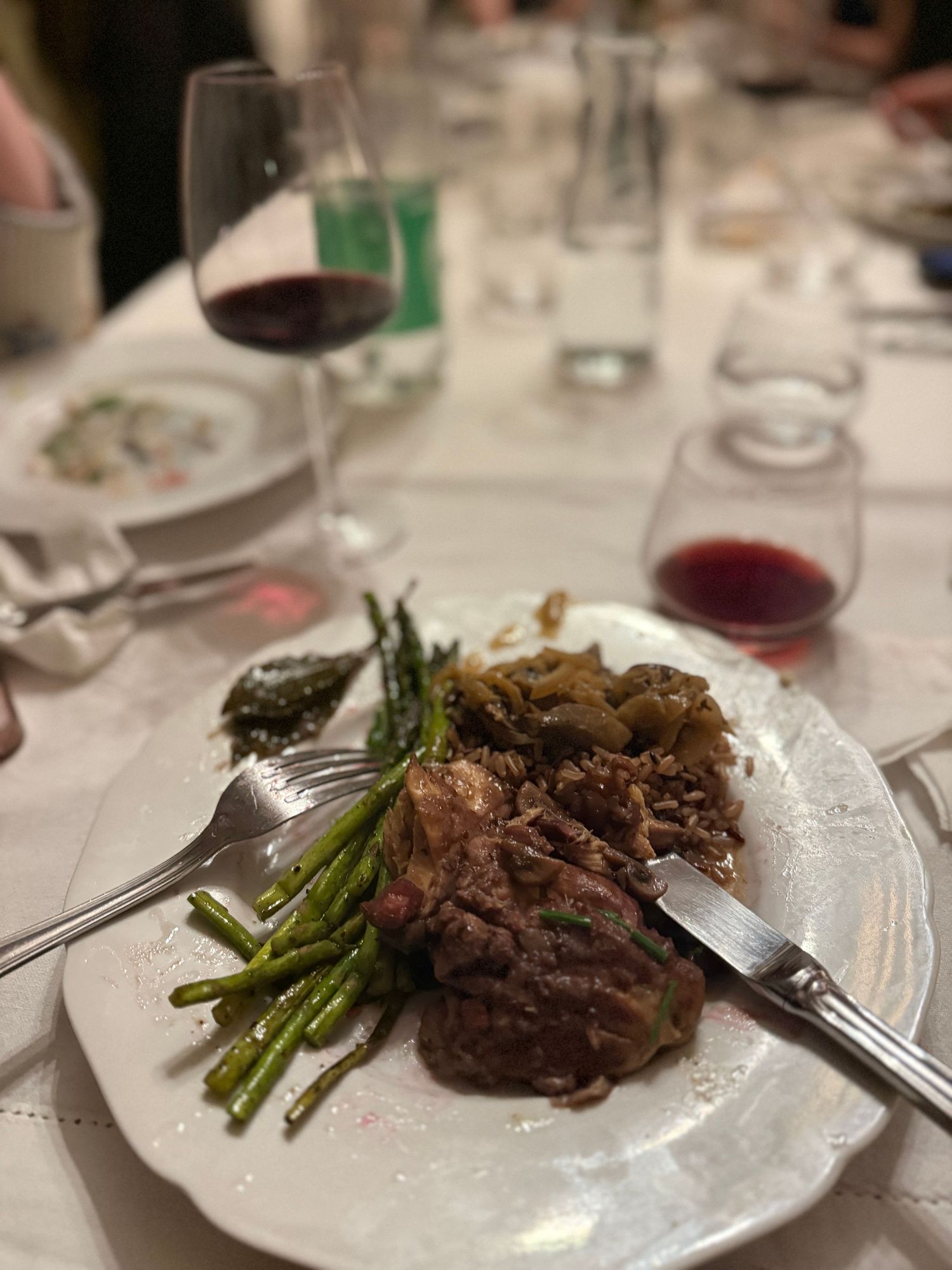 Grilled steak with asparagus and sauce on white plate alongside red wine glass.