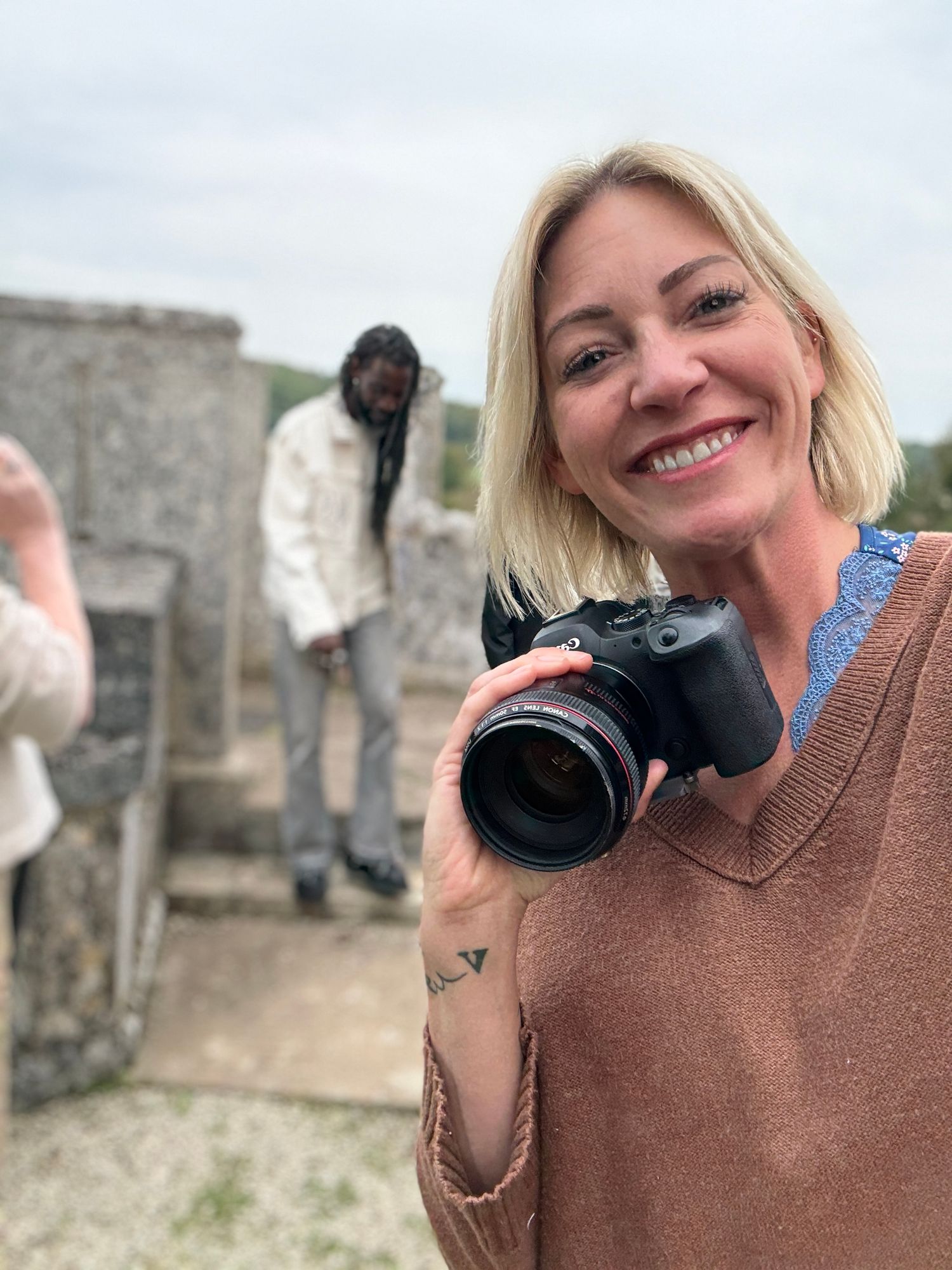 Photographer with professional camera standing near stone ruins on cloudy day.