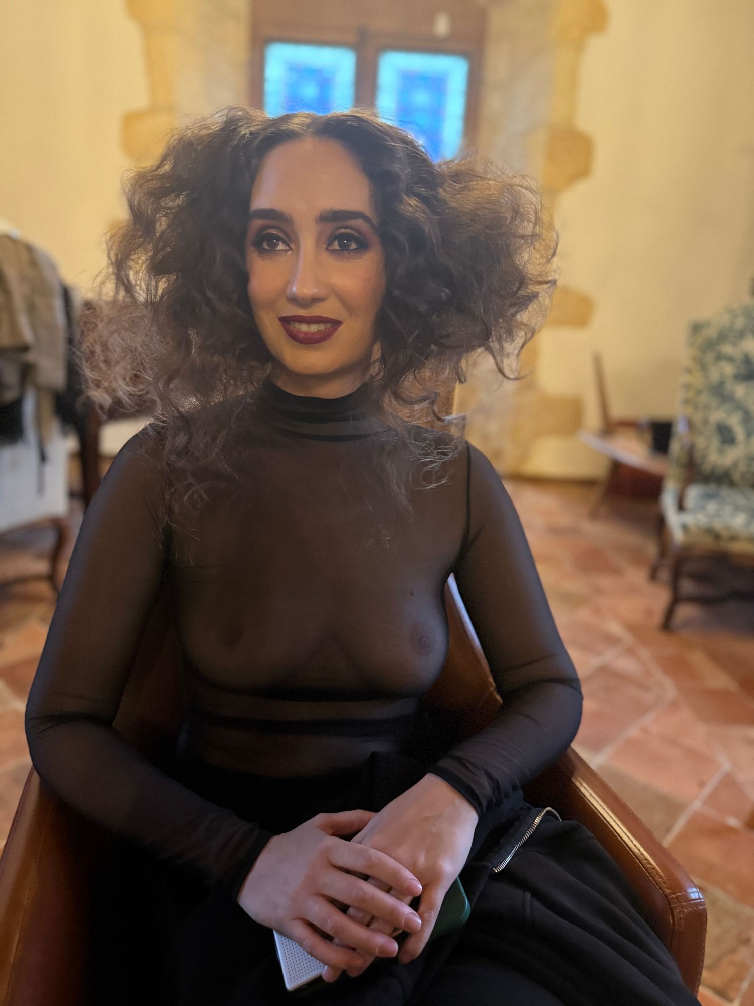Person in a dark turtleneck sitting in a warmly lit room with textured walls.