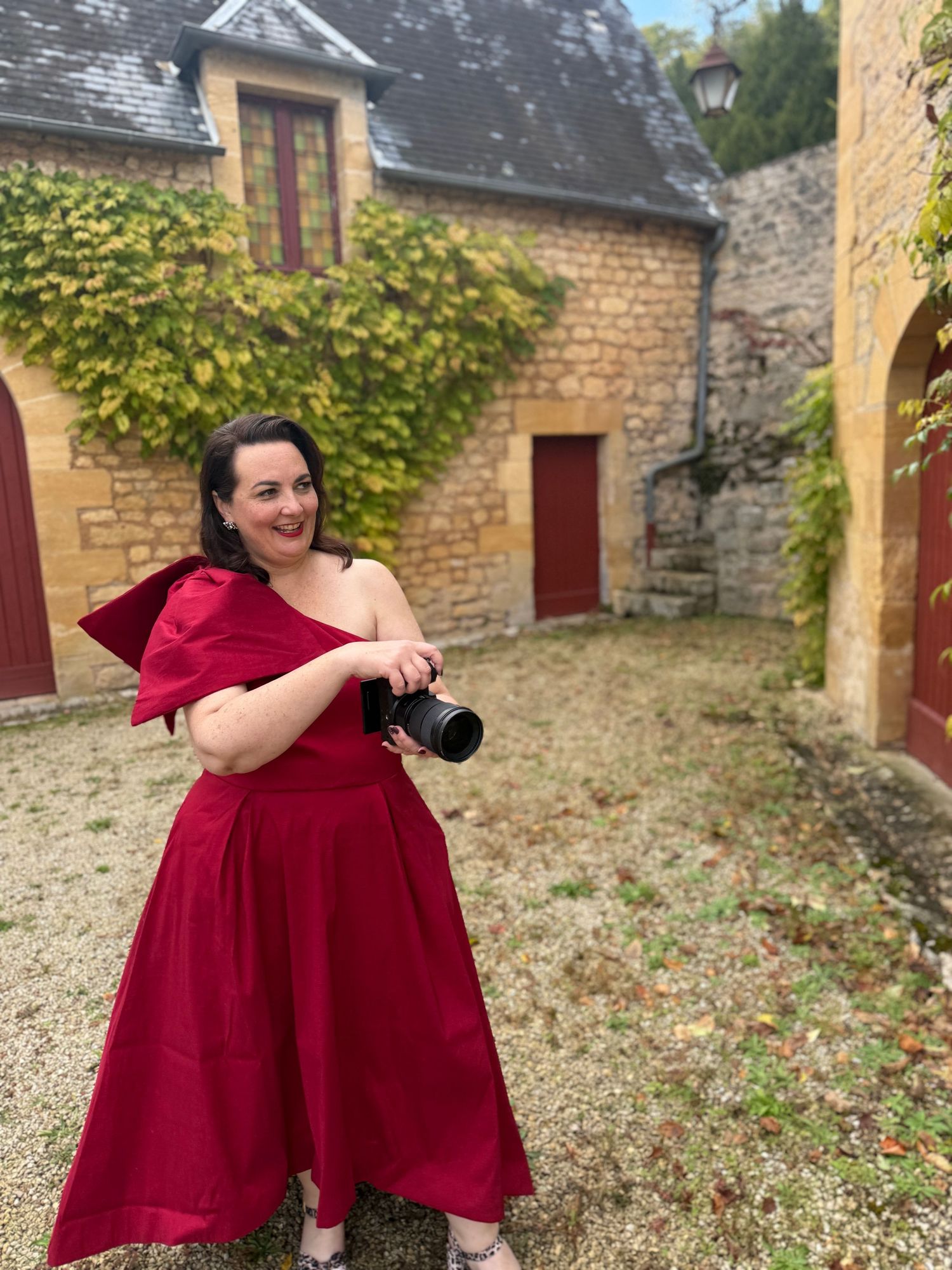 Person in a burgundy dress sitting outdoors against stone building walls.