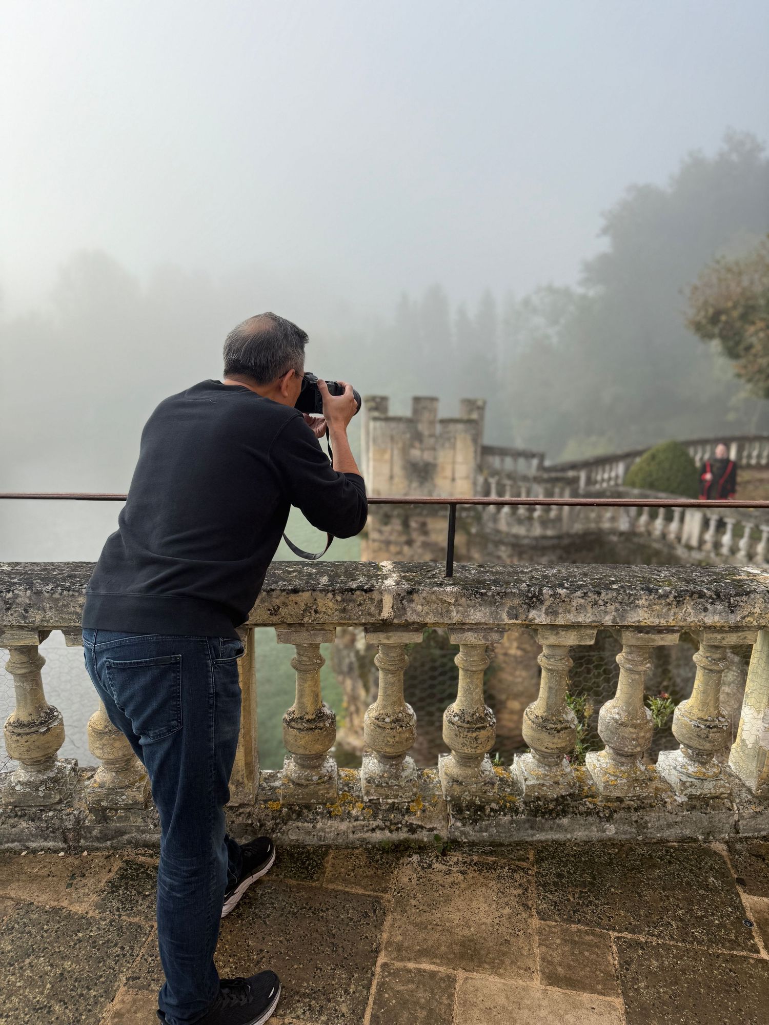 Photographer taking pictures over an ornate stone balustrade on a misty morning.