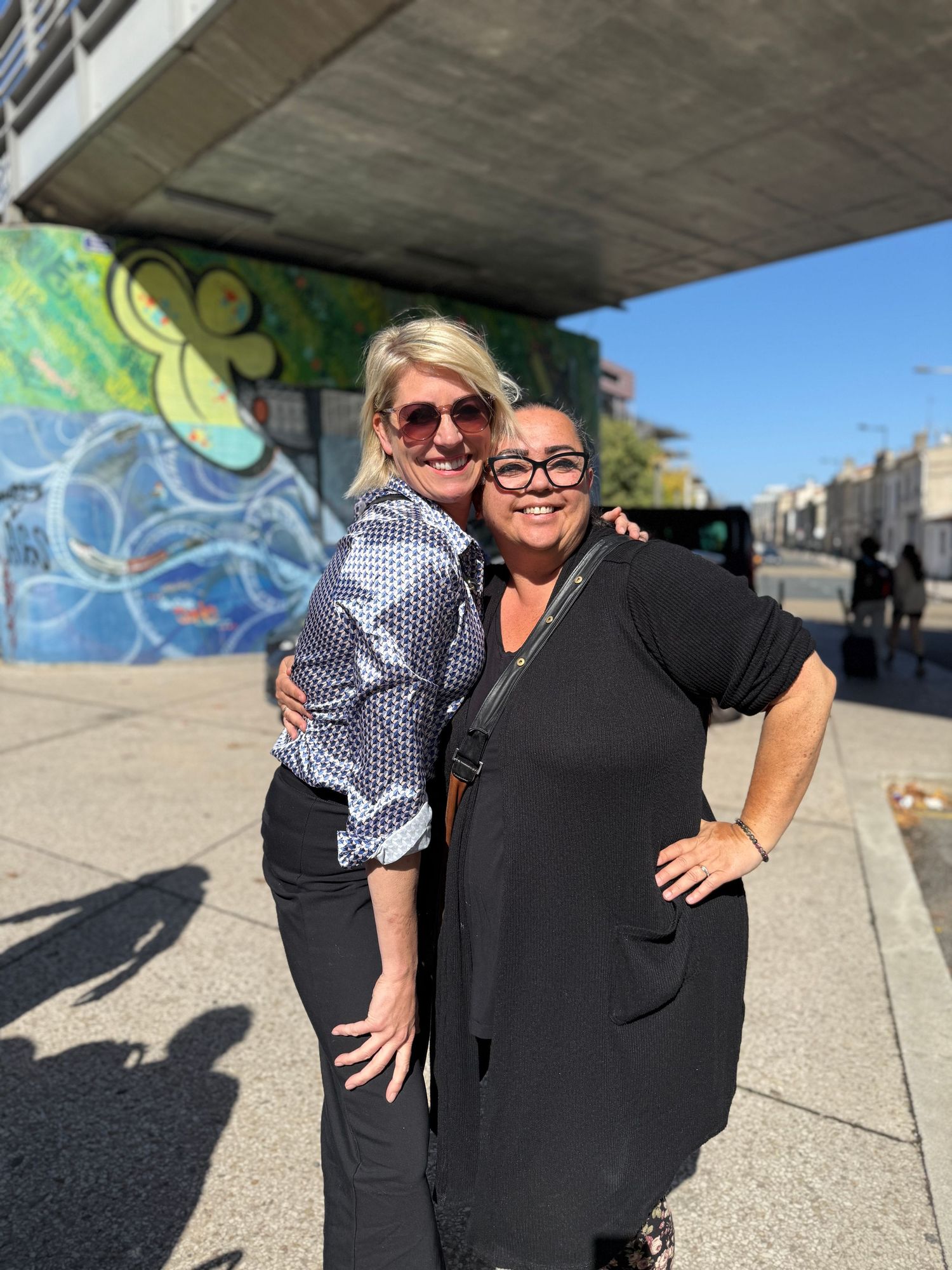 Two people posing playfully together against a colorful street art mural background.