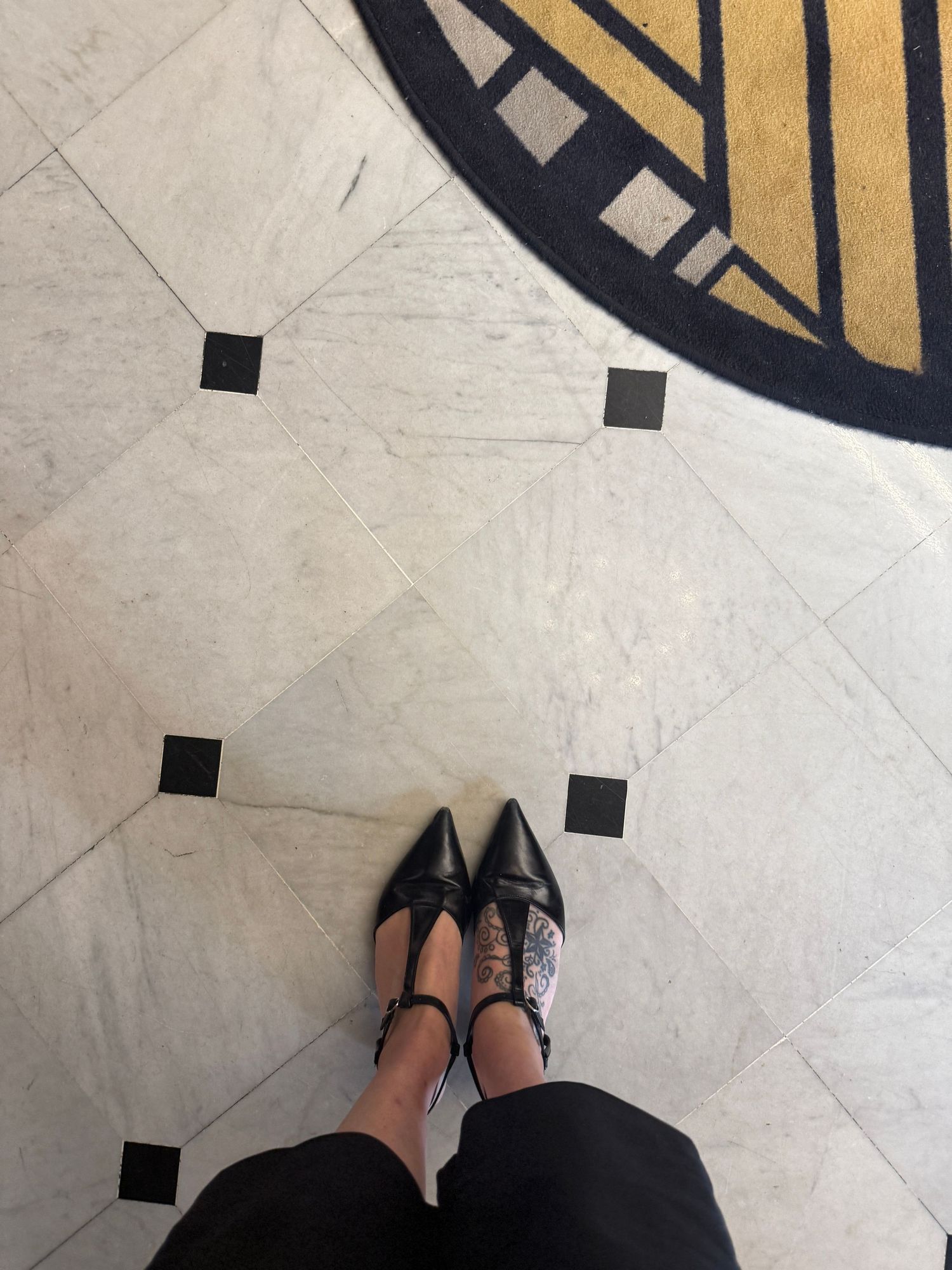 Black pointed ballet flats shown on marble flooring with geometric patterns.