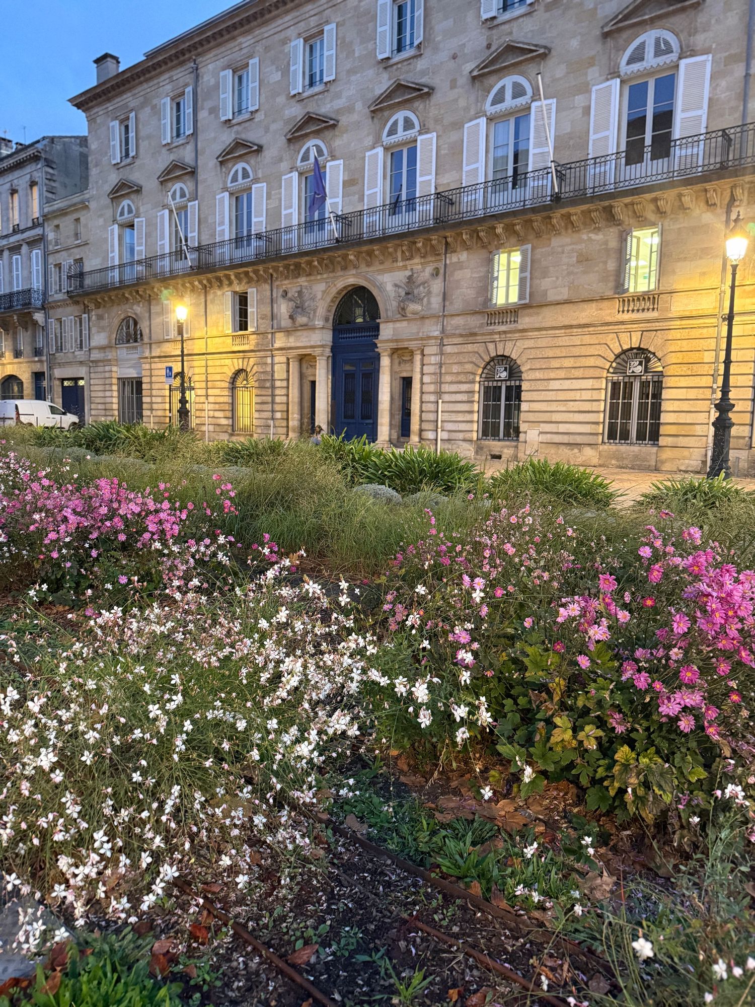 Beautiful flower garden with pink and white blooms in front of a historic stone building at dusk.
