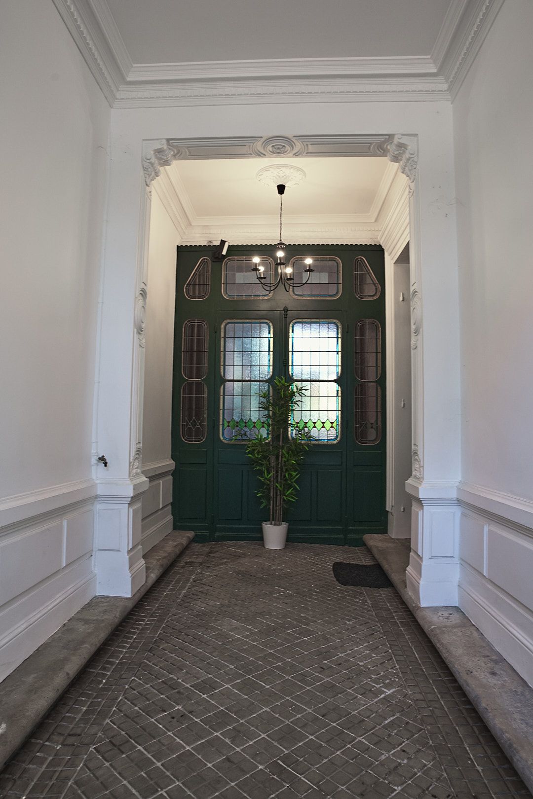 Elegant entrance hallway with green doors and white walls featuring classical architectural details.