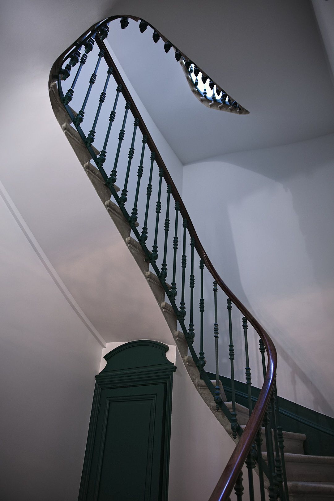 Dark green painted staircase with ornate iron railings in a historic building.