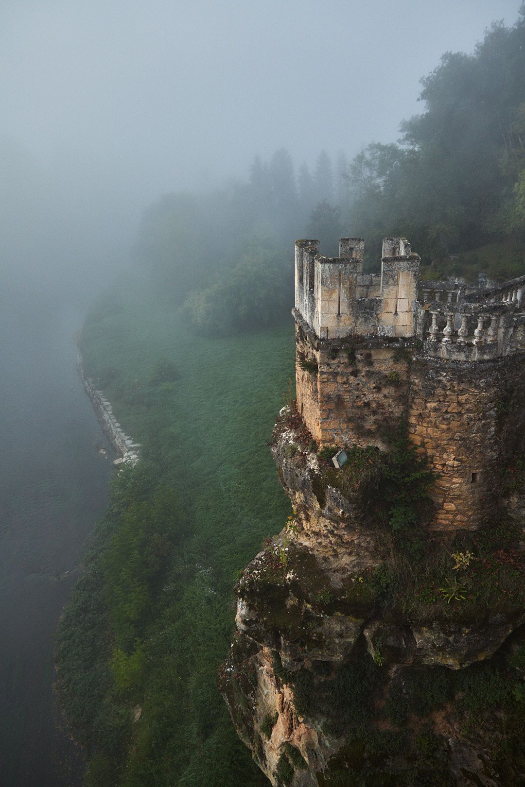 Dramatic foggy views of ancient stone fortress walls perched on steep cliffs.