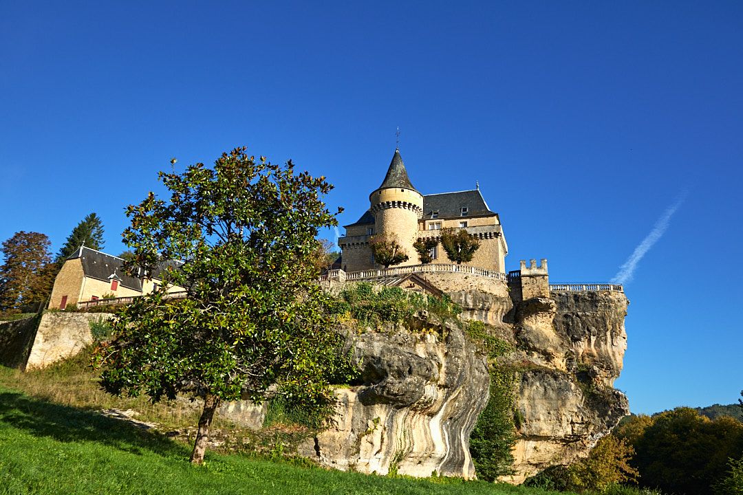 Historic castle perched on limestone cliffs against bright blue sky.