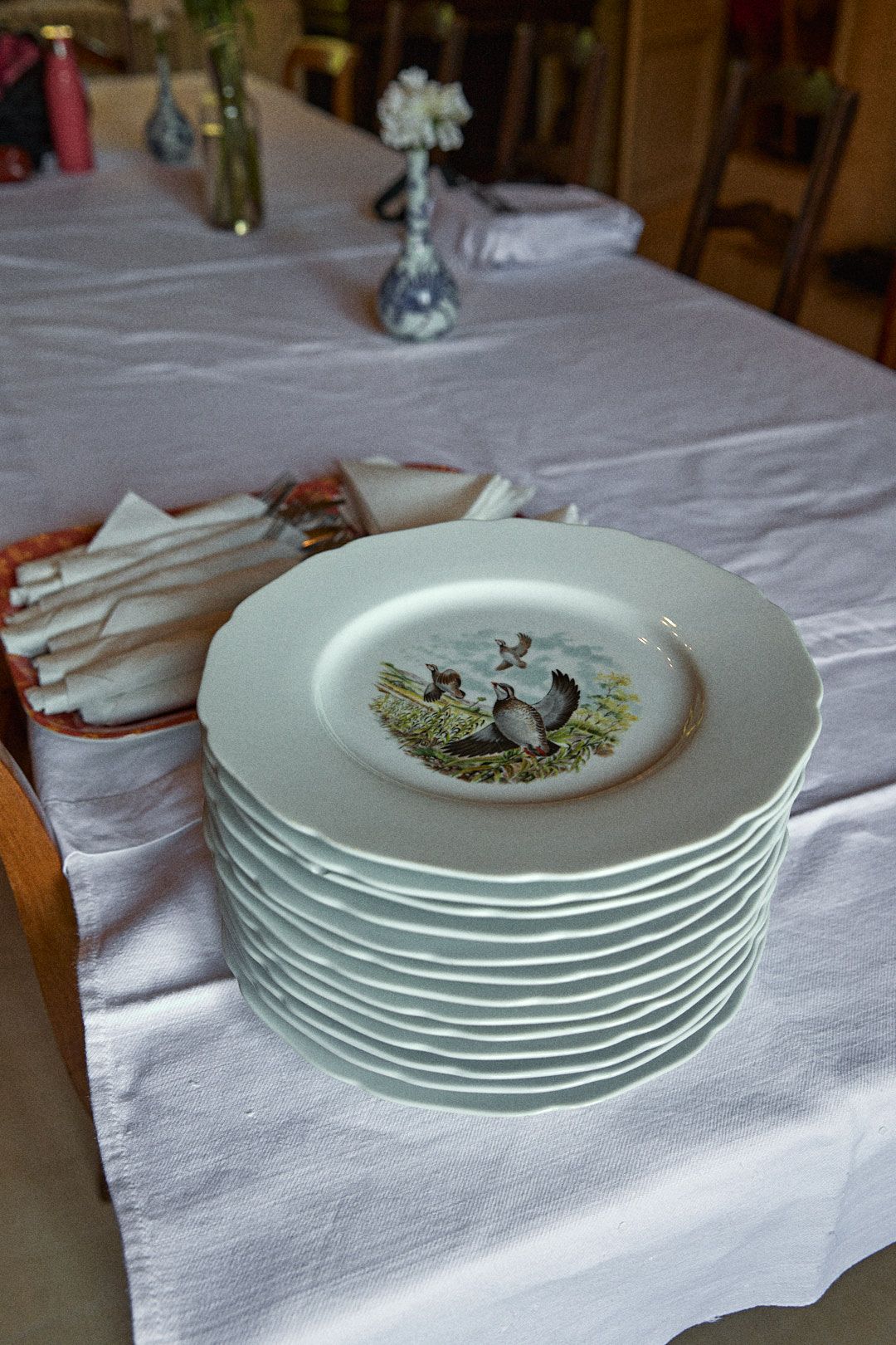 Stack of vintage decorative plates with pastoral scenes on white tablecloth.