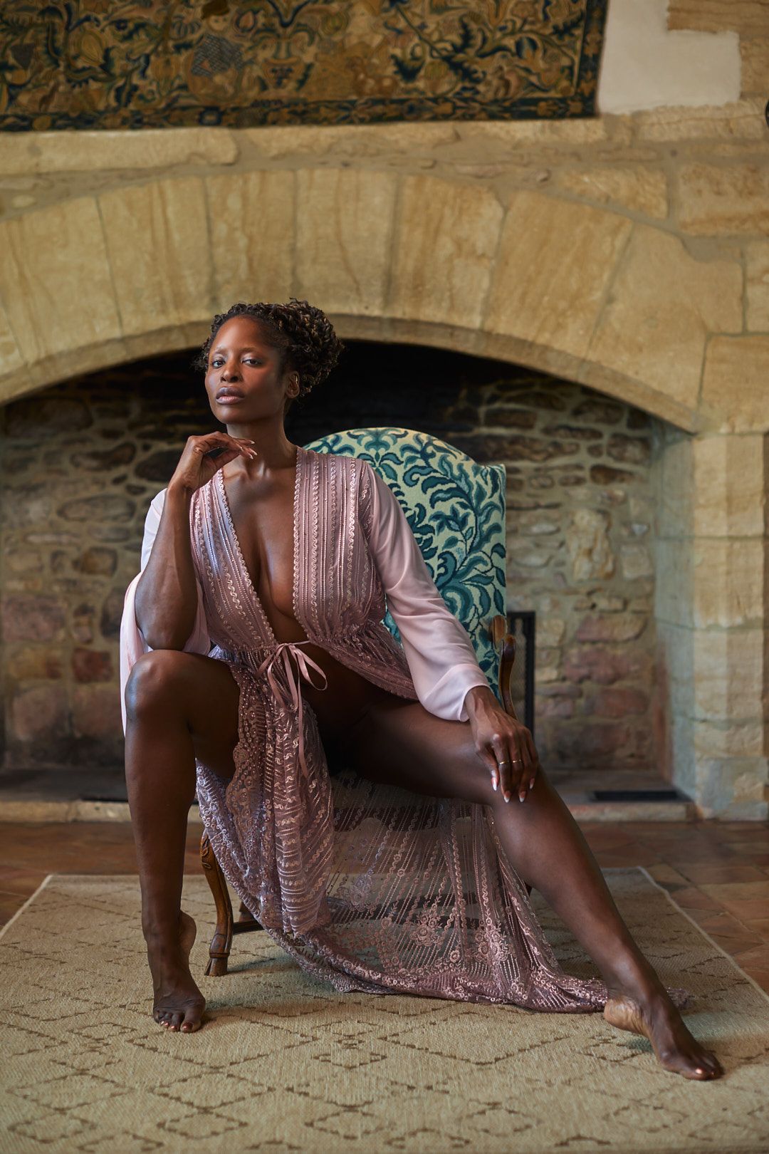Person in a pink dress reclining on stone floor in front of historic stone archway.