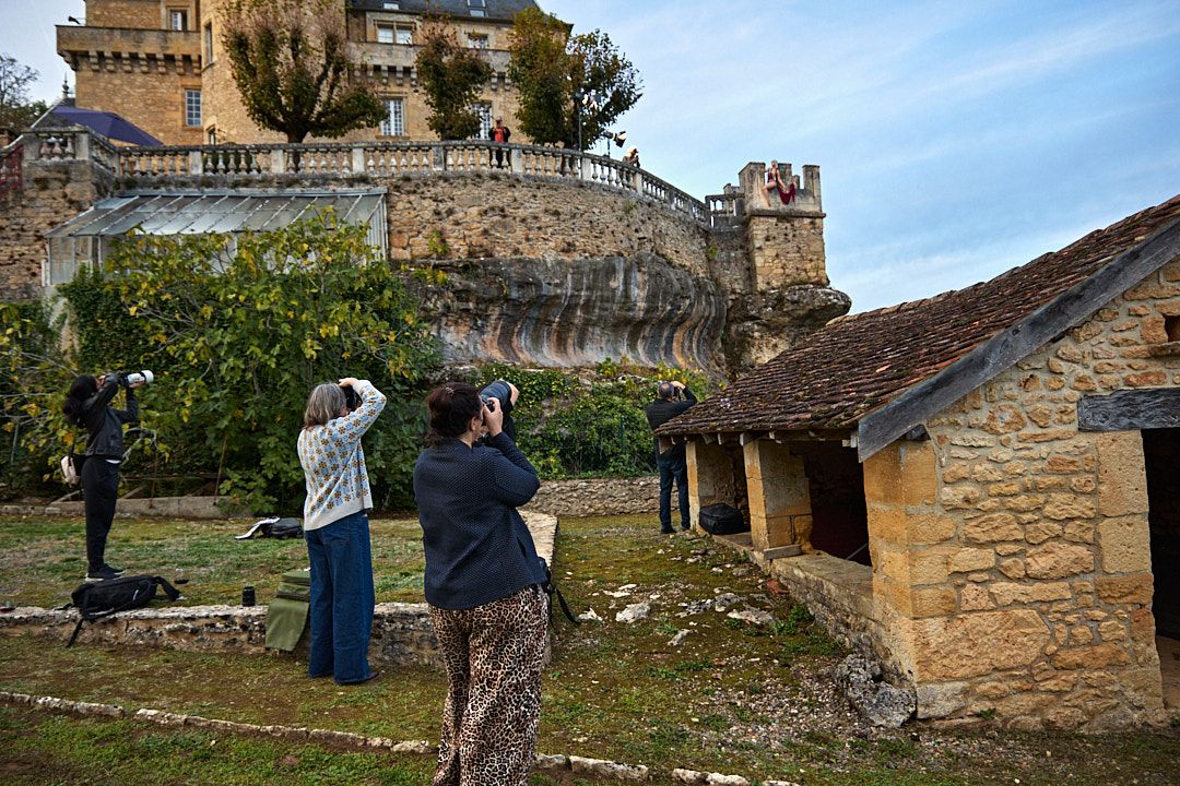 Tourists taking photos of an ancient stone castle perched on a hillside under blue skies.
